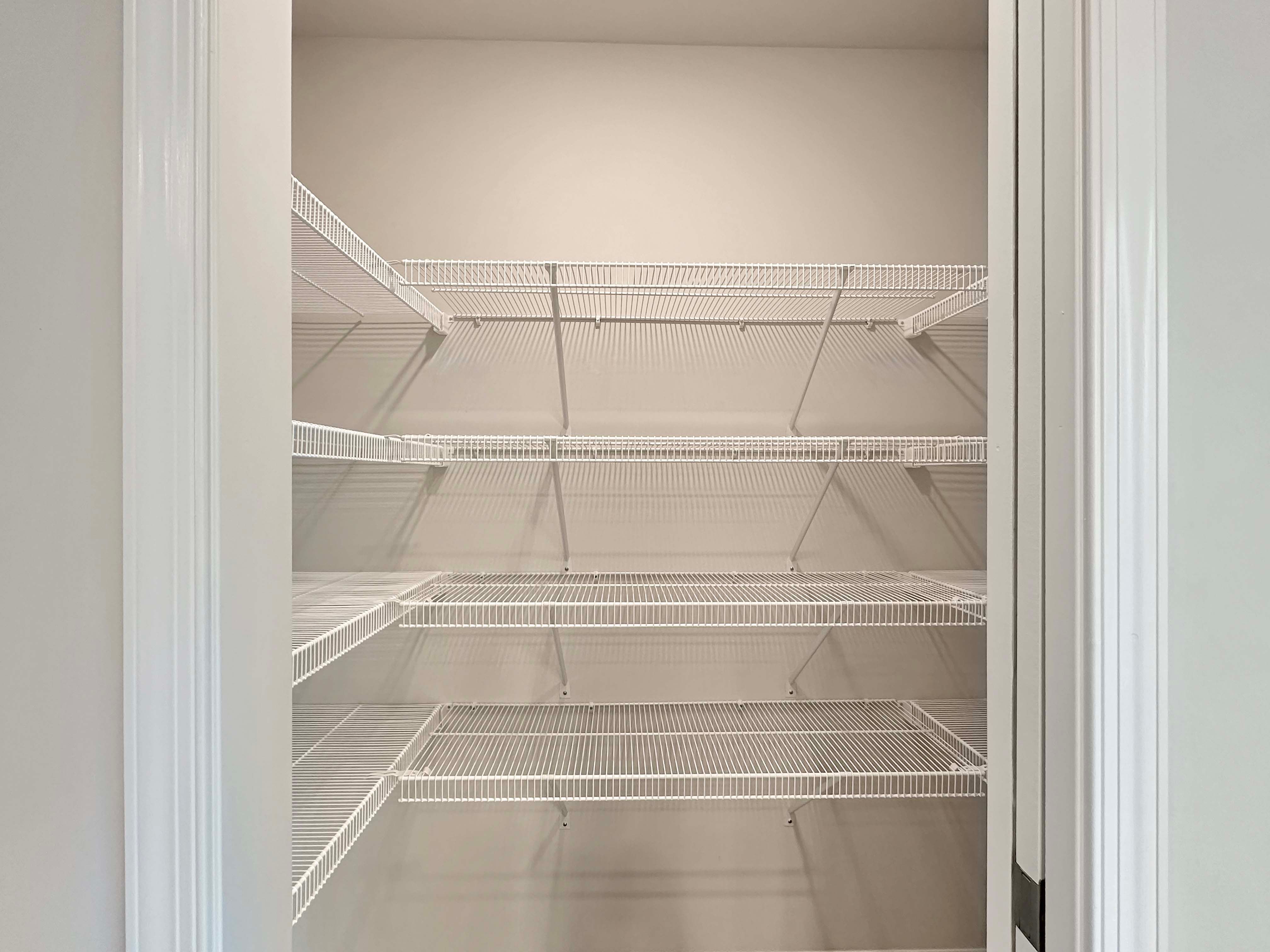 Walk-in pantry with multiple white wire shelves for storage.