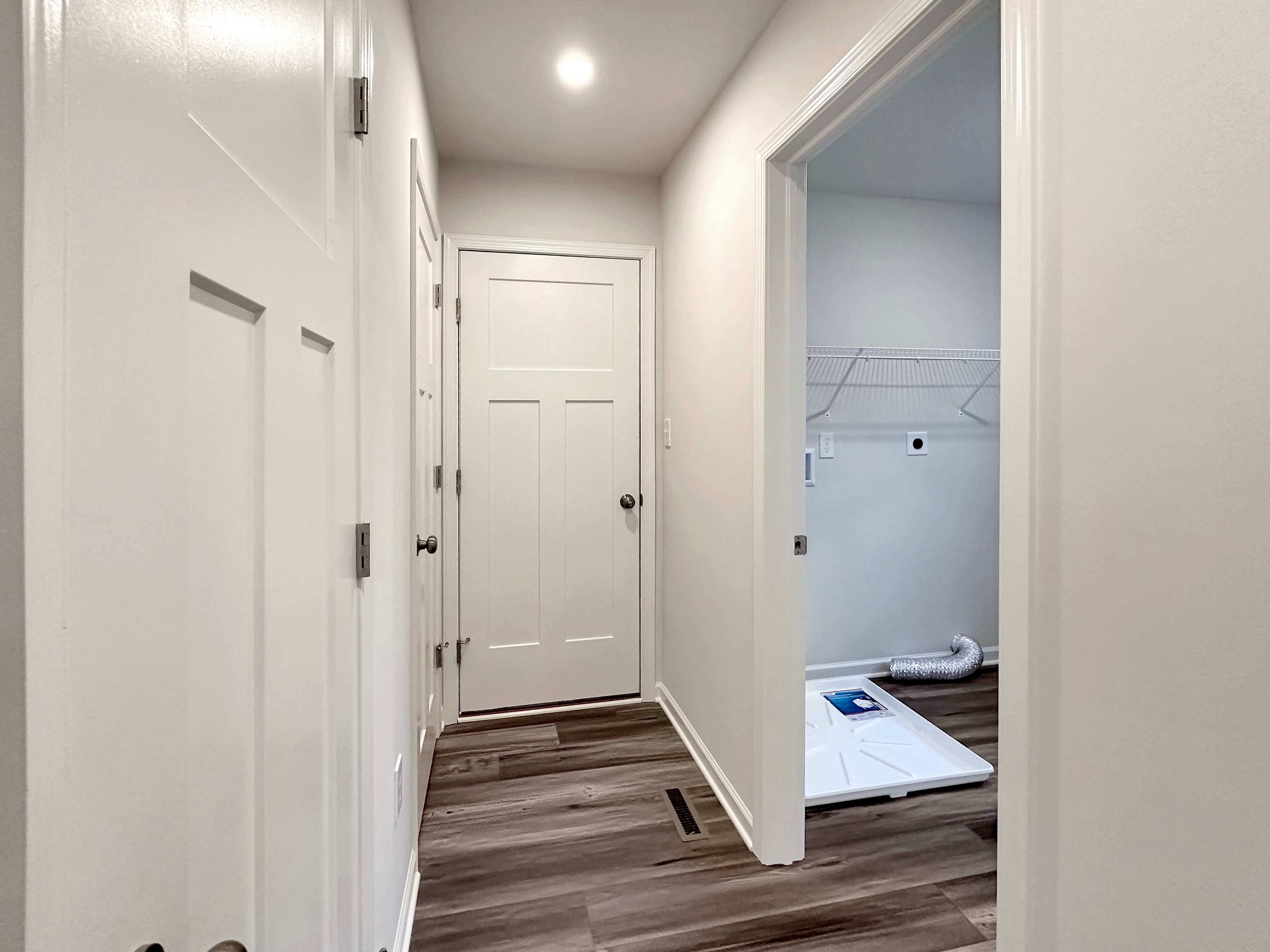 Hallway leading to laundry room with hardwood flooring, white doors, and a closet for added storage space.