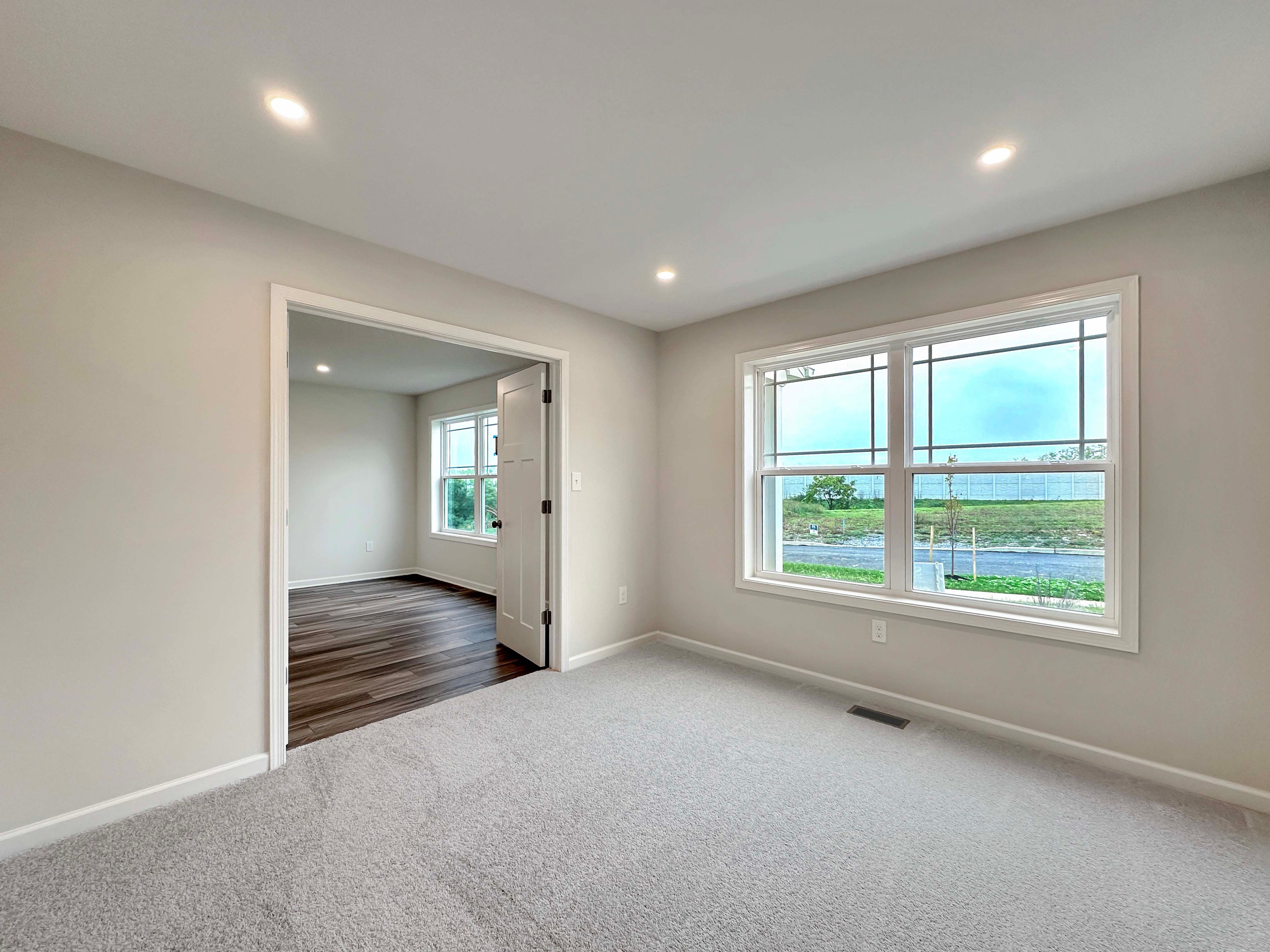 Bright den with wide window, carpet flooring, and view of the front yard, ideal for a home office or study.