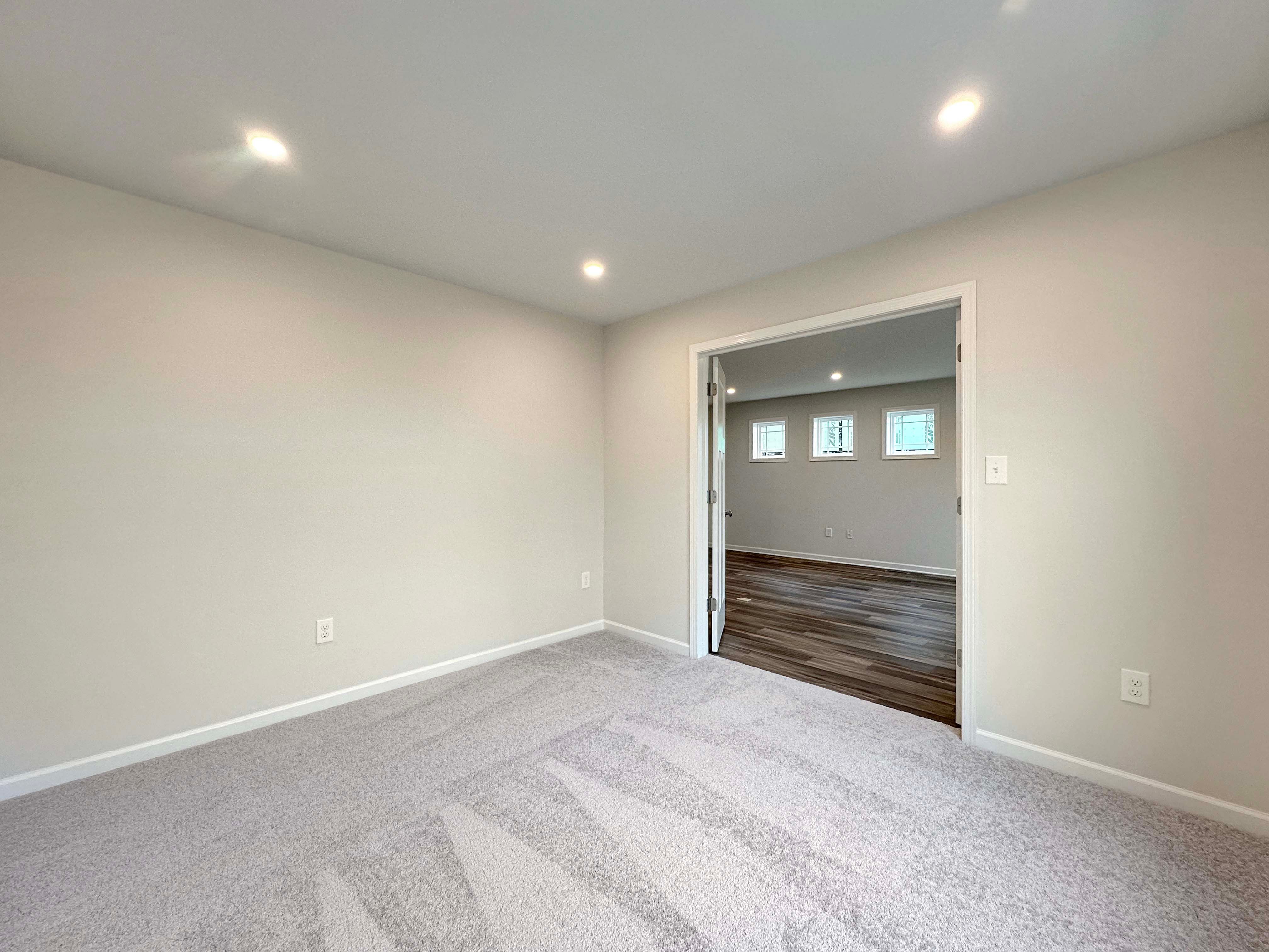 Spacious den with recessed lighting, double doors, and a view into an adjacent room with hardwood floors.