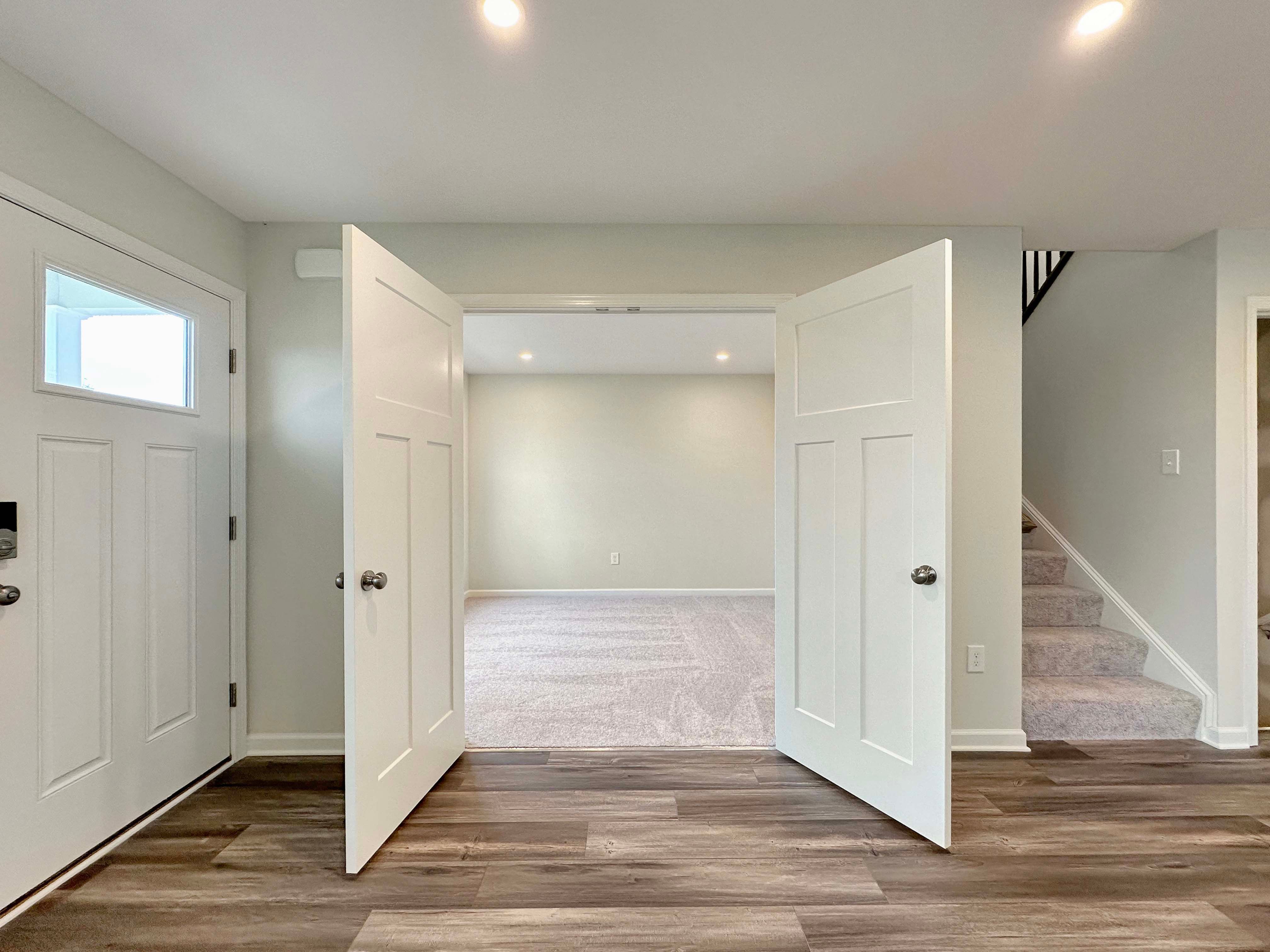 Entrance to a den with double doors, leading to a carpeted room, featuring a view of stairs and hardwood floors.