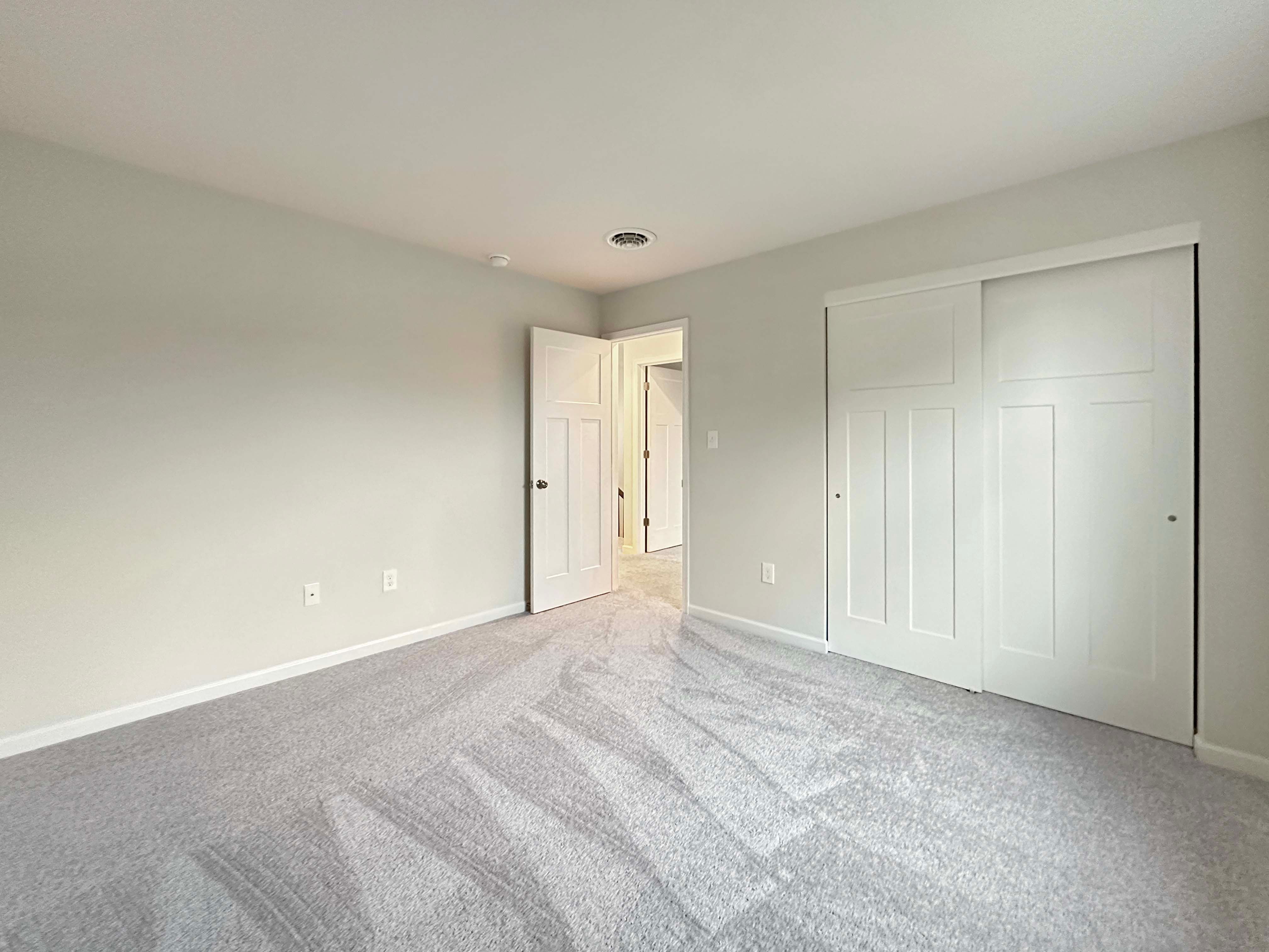 Unfurnished bedroom with double closet doors, carpeted floor, and doorway leading to a hallway.