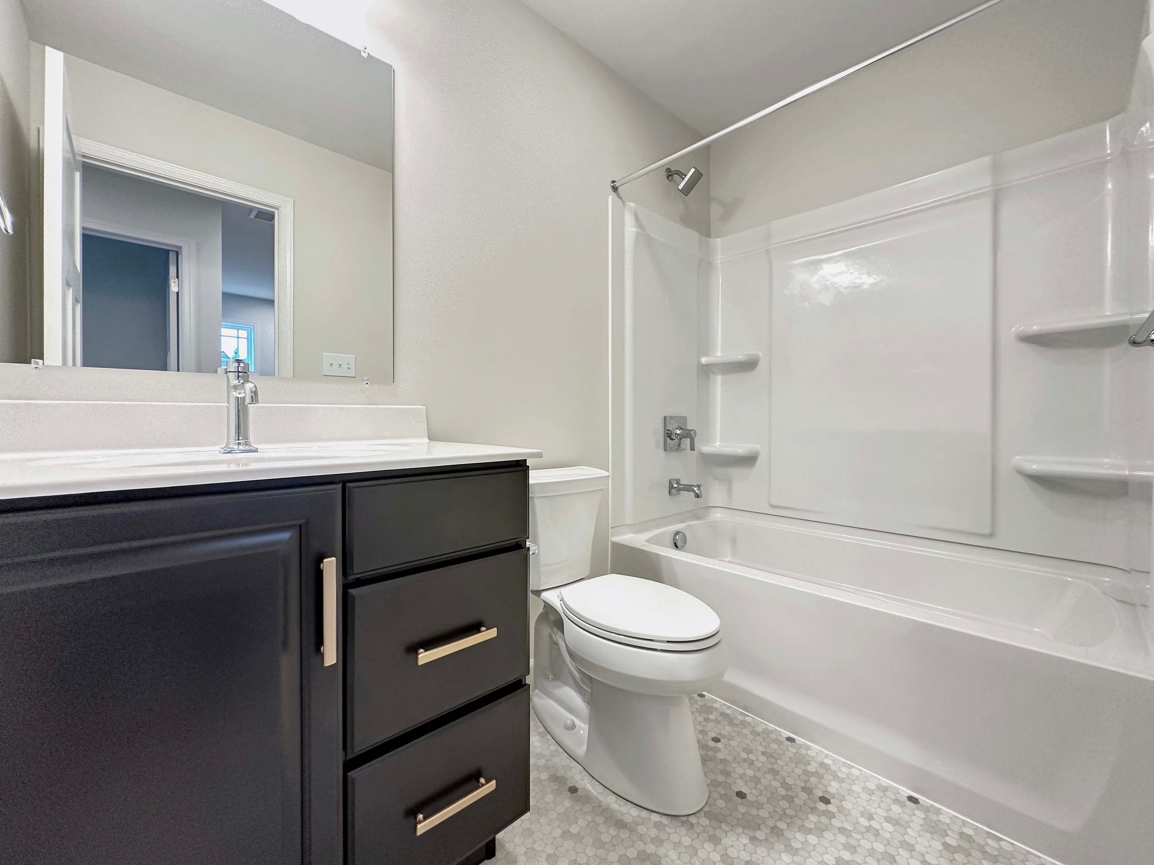 Bathroom featuring a dark vanity, white countertop, bathtub with shower, and hexagon-tiled flooring.