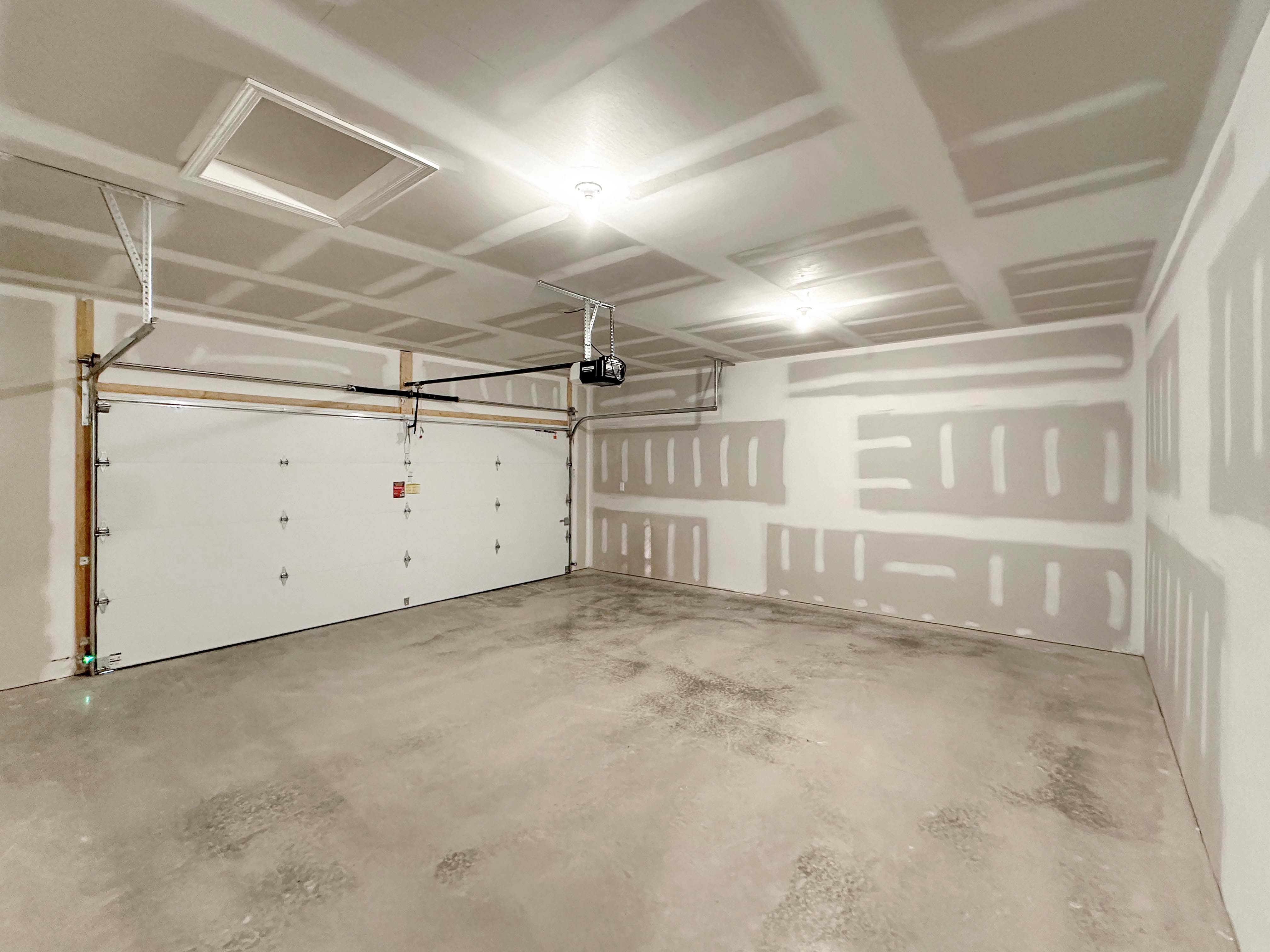 Spacious two-car garage with unfinished drywall and a concrete floor, featuring a ceiling-mounted garage door opener.