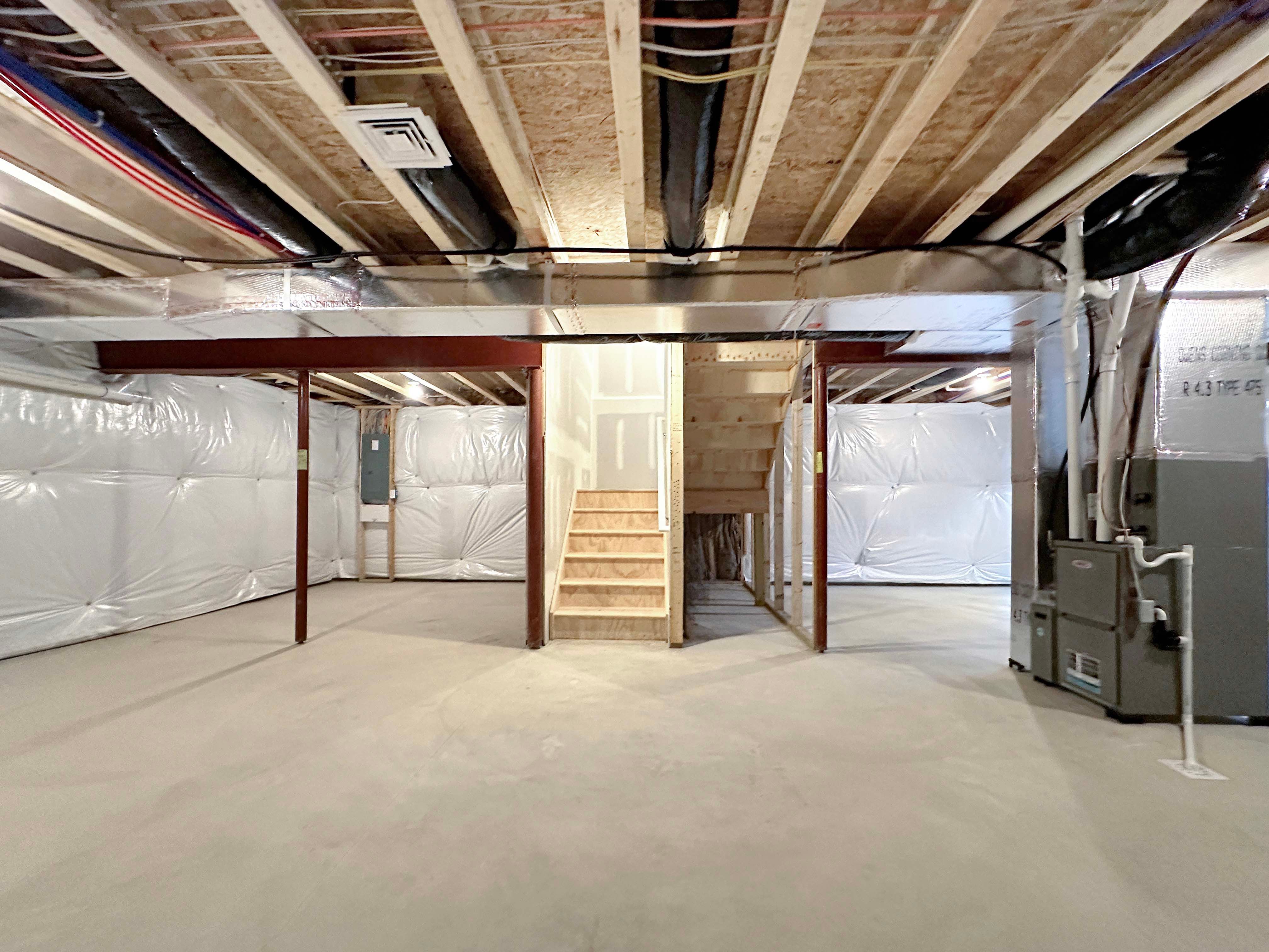 Spacious basement with a large open layout, exposed beams, support columns, ,an electrical panel, and stairs to main level.