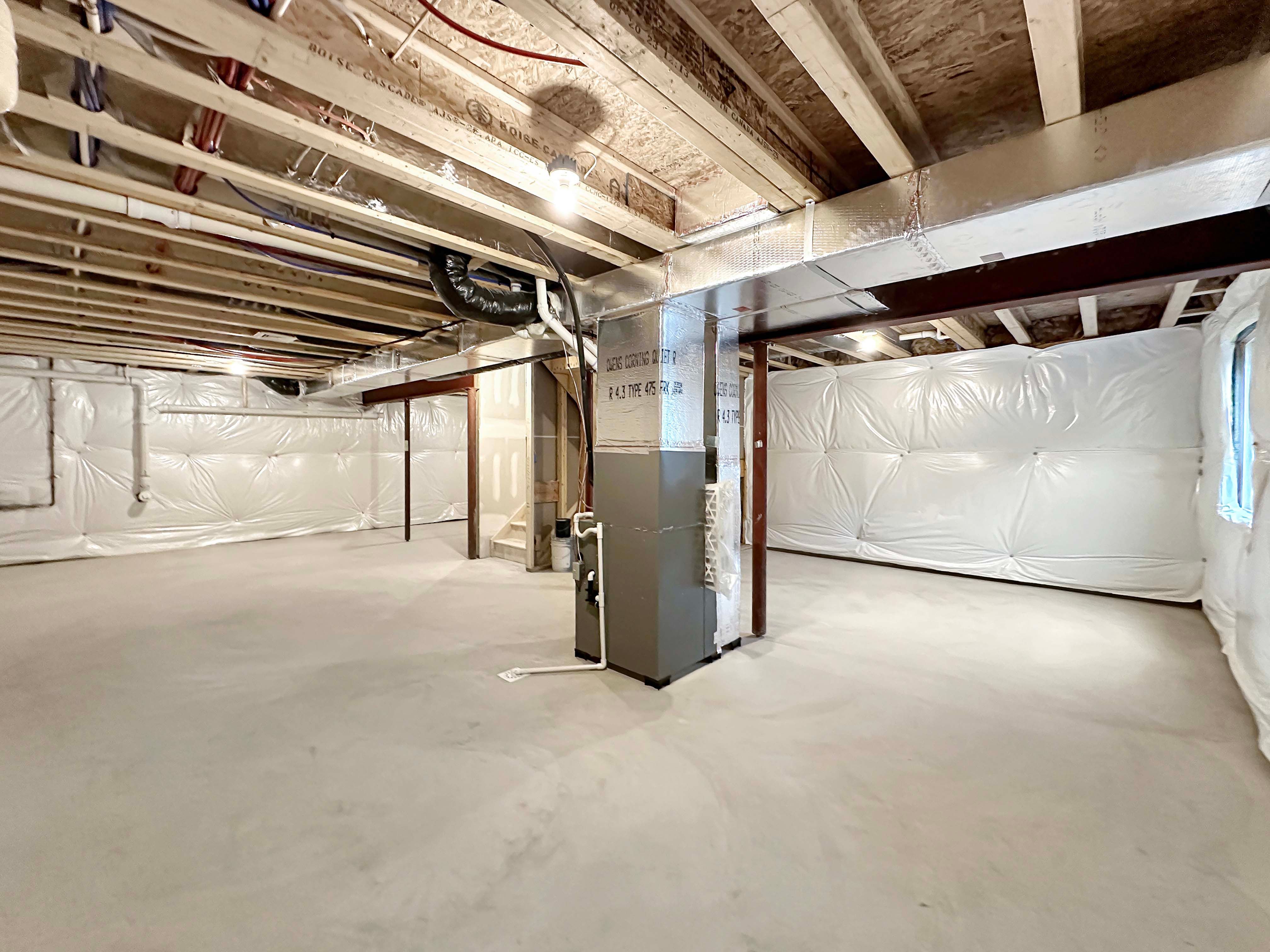 Unfinished basement with exposed ceiling and HVAC system, offering a wide, open space for future use