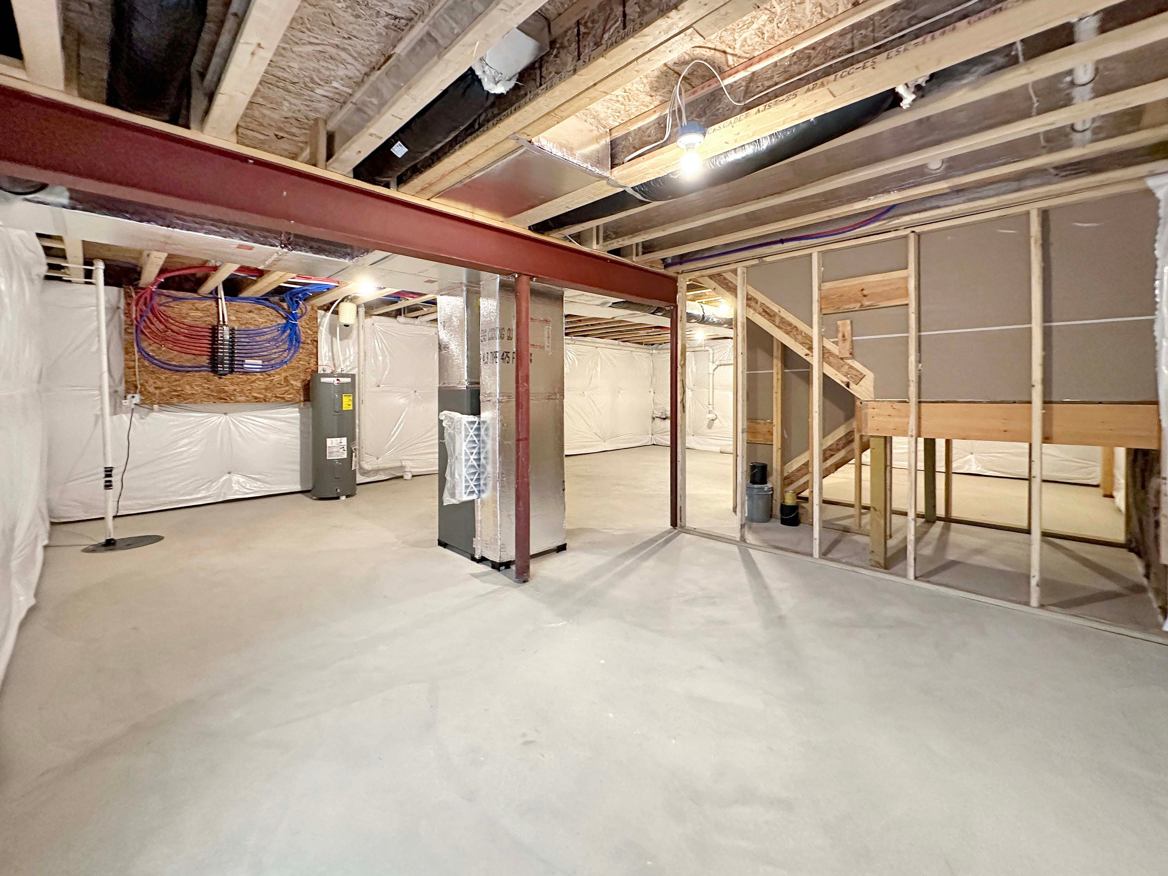 Open, unfinished basement featuring visible support columns and utilities, with egress window providing natural light