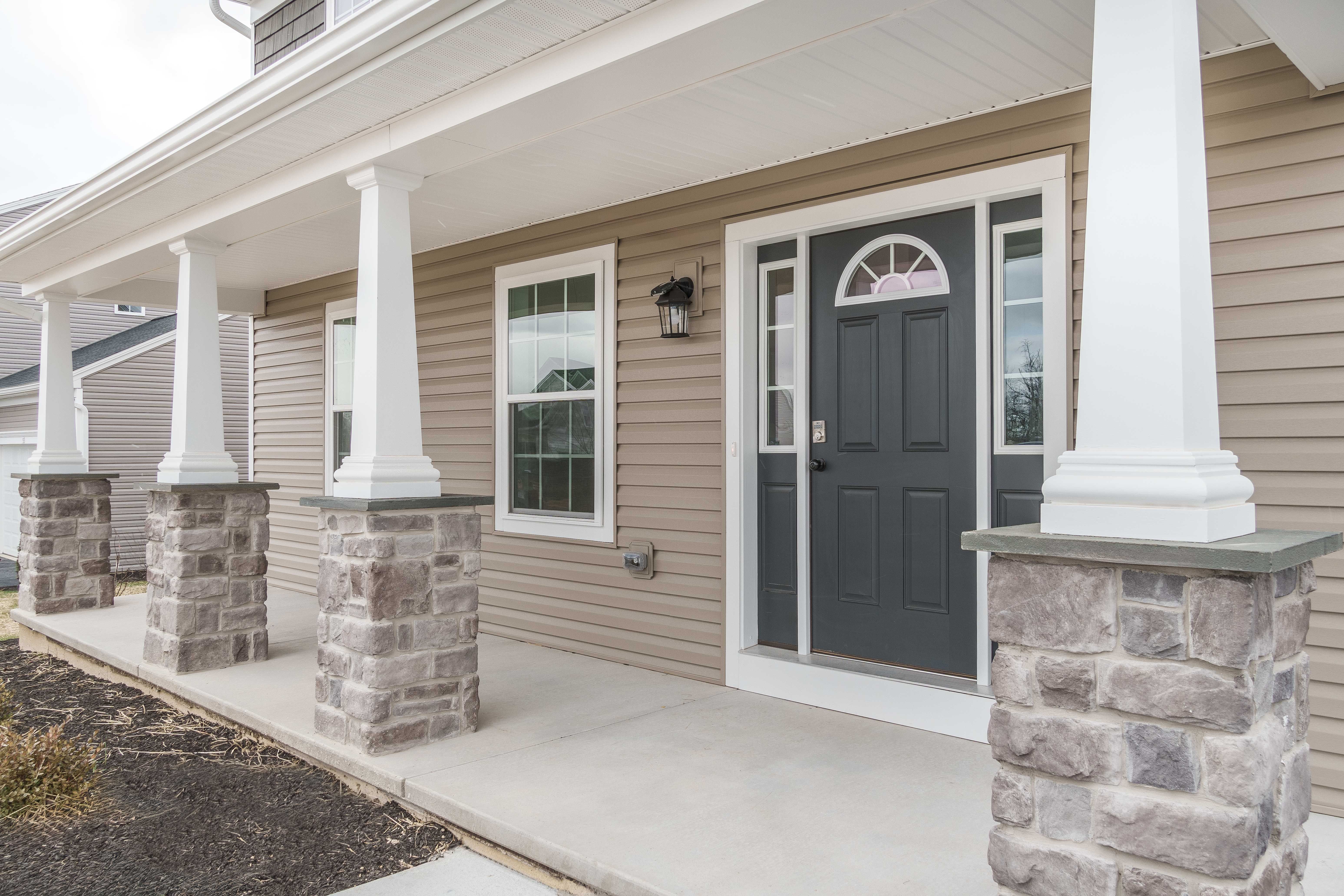 Covered front porch with stone column bases, white pillars, and a gray front door featuring glass sidelights.