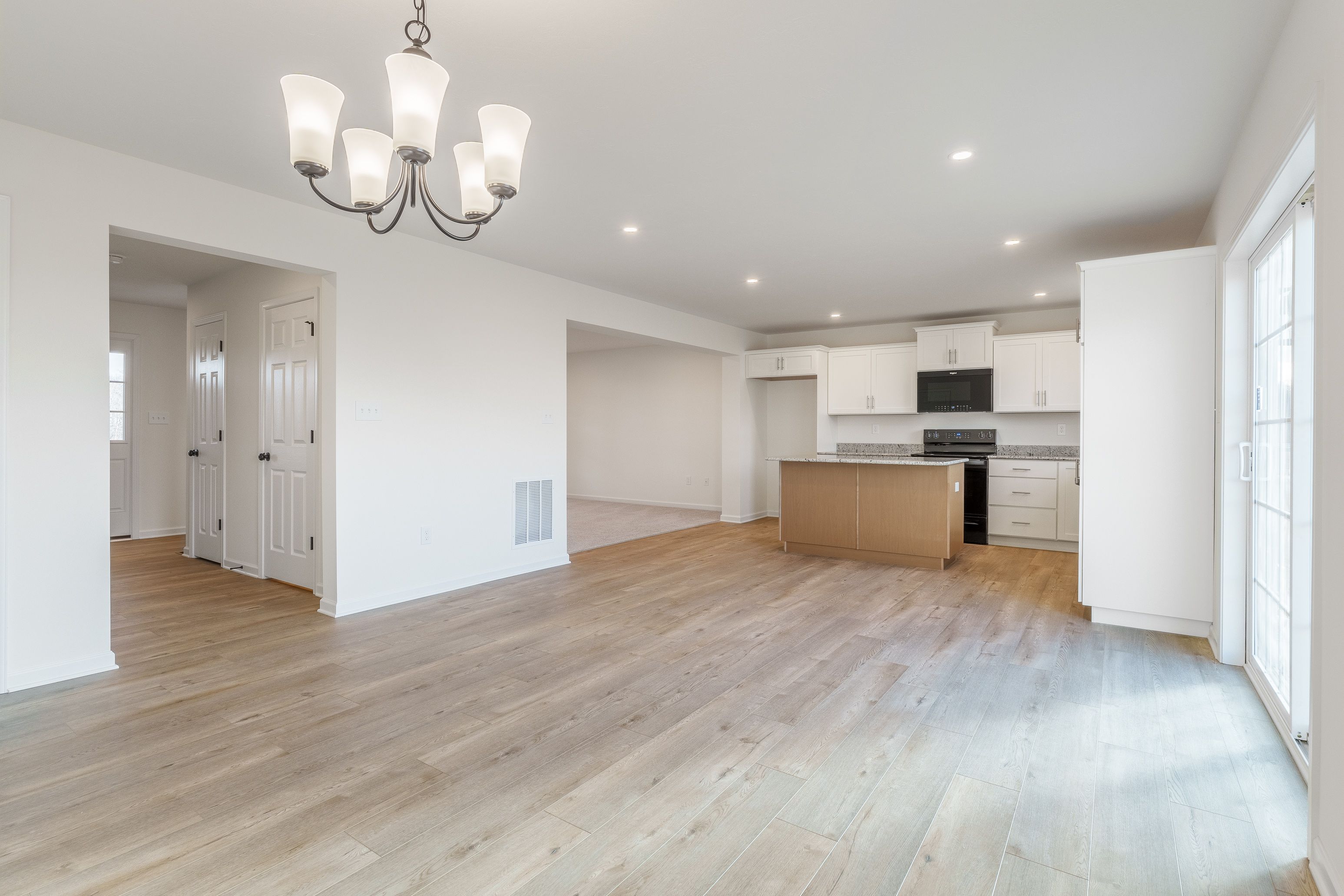 Modern kitchen with white cabinets, granite countertops, stainless steel appliances, and luxury vinyl plank flooring.