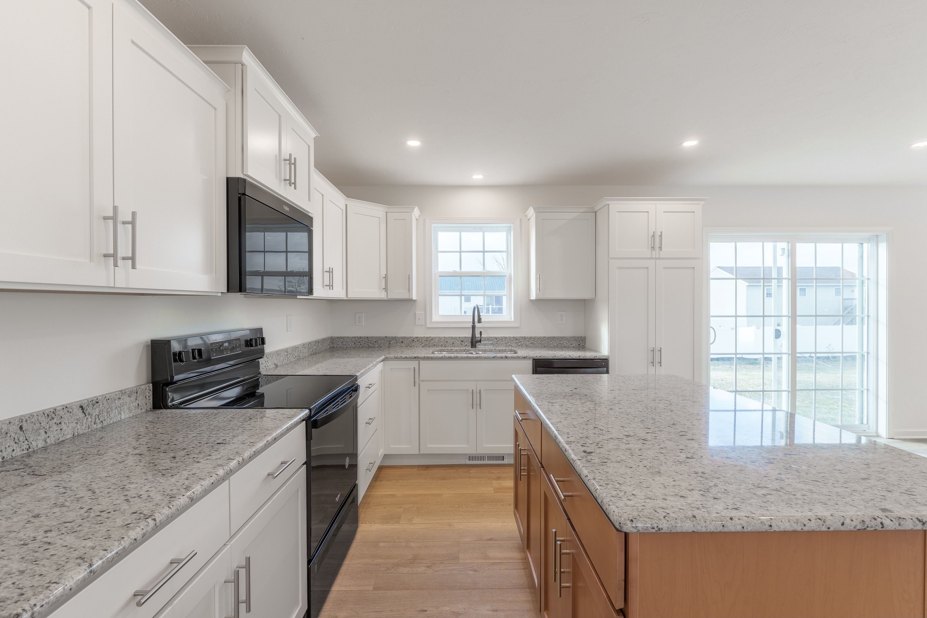 Kitchen featuring white cabinets, granite countertops, black stainless steel appliances, and a window with a view outside.