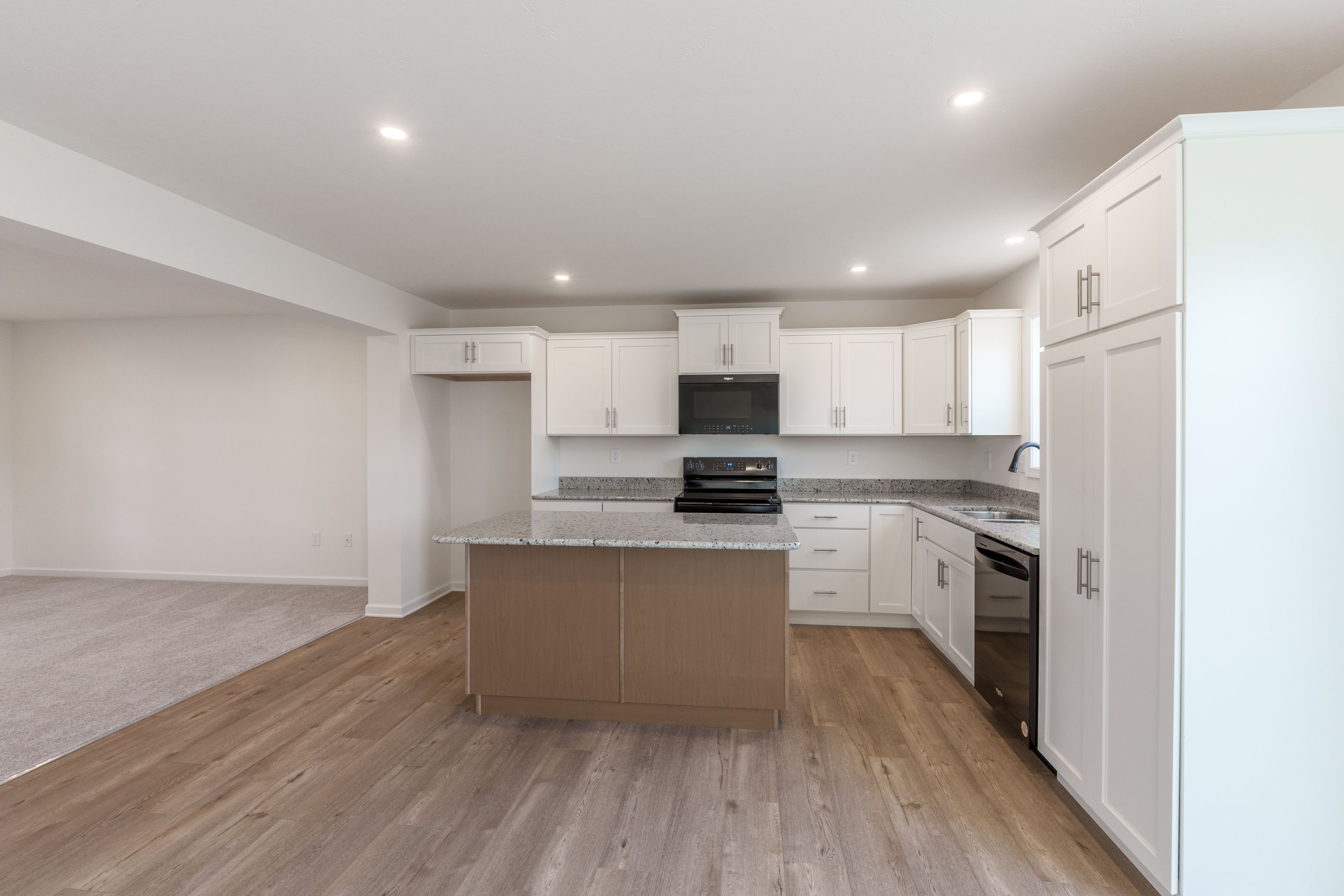 Bright kitchen withblack stainless steel appliances, white cabinets, granite countertops, and an open layout to the dining area.