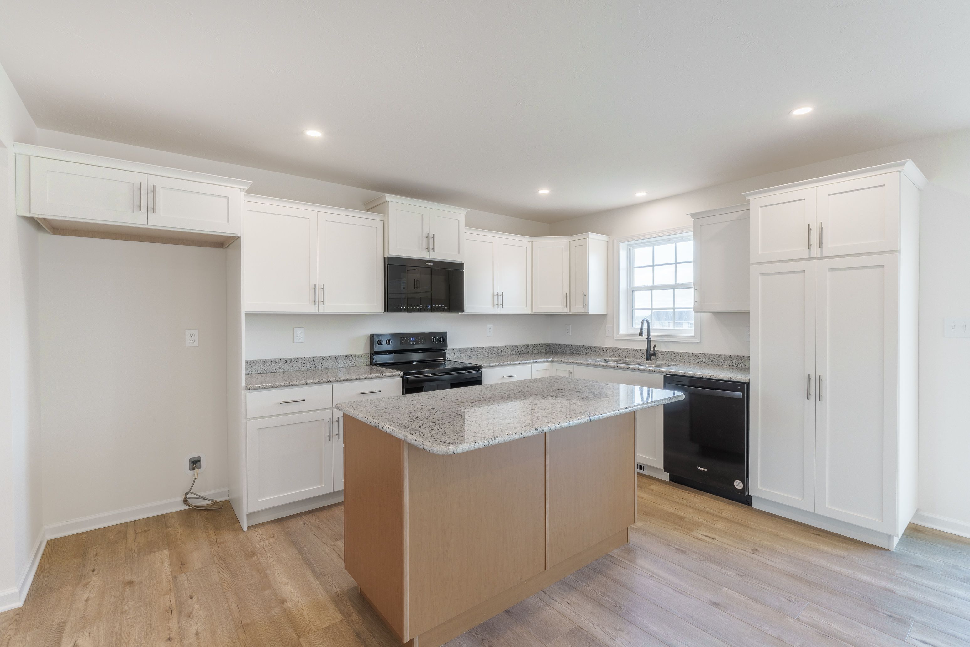 View of the kitchen with white cabinetry, granite countertops, and modern black stainless steel appliances. Spacious island area.