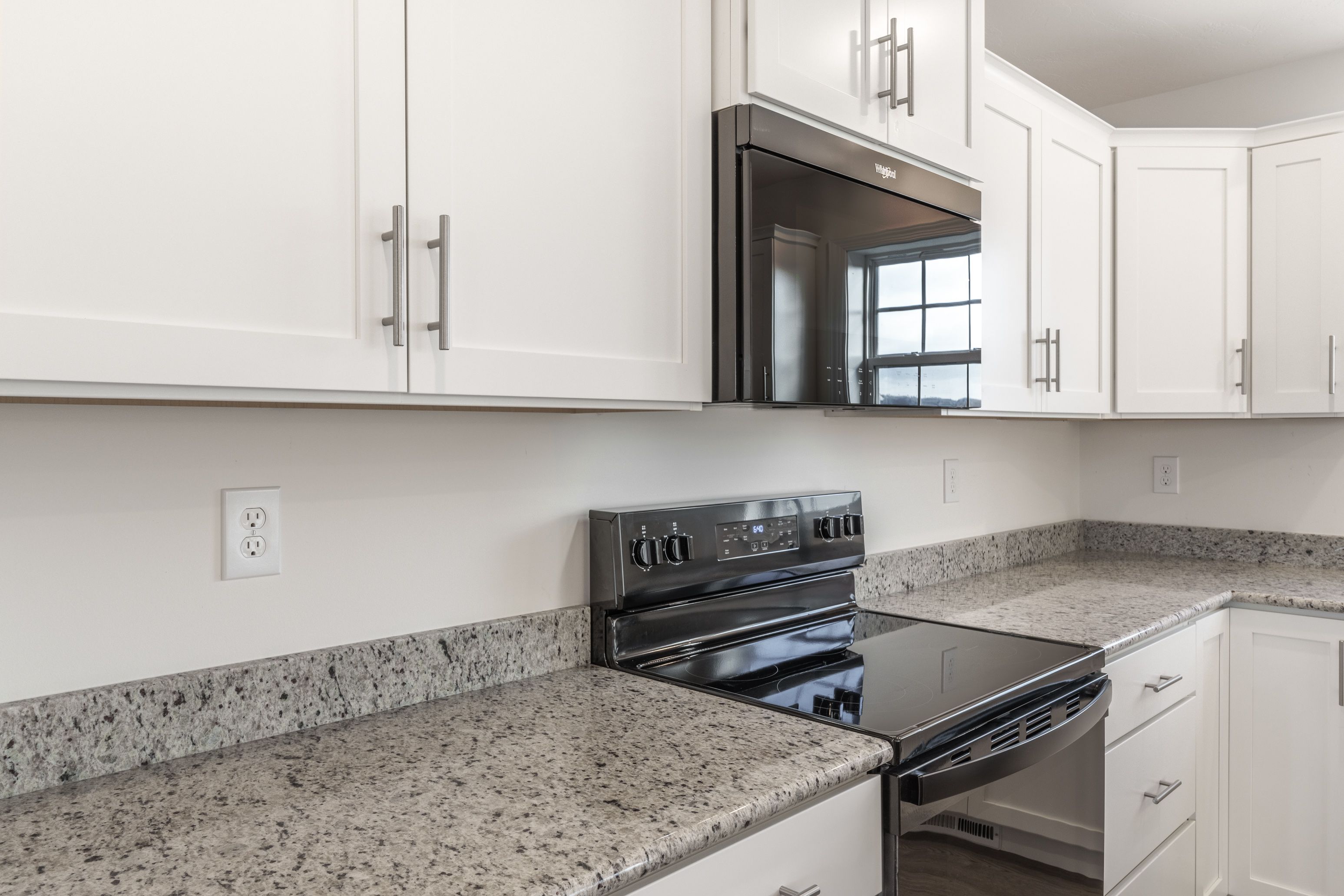 Spacious kitchen with white cabinetry, granite countertops, and sleek black stainless steel appliances with plenty of counter space.