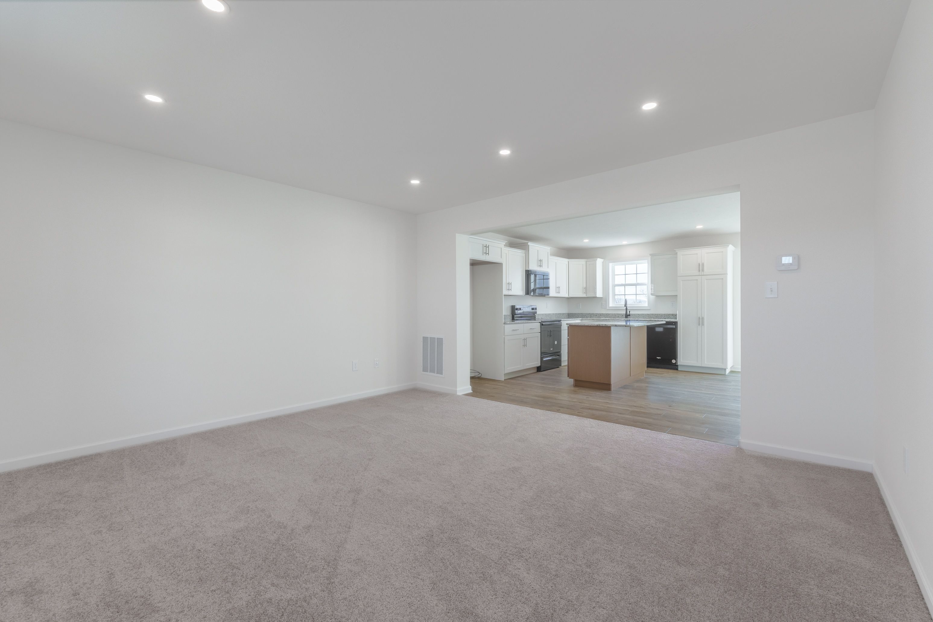 Family room with light carpet, natural light from windows, and a seamless transition to the adjacent kitchen.