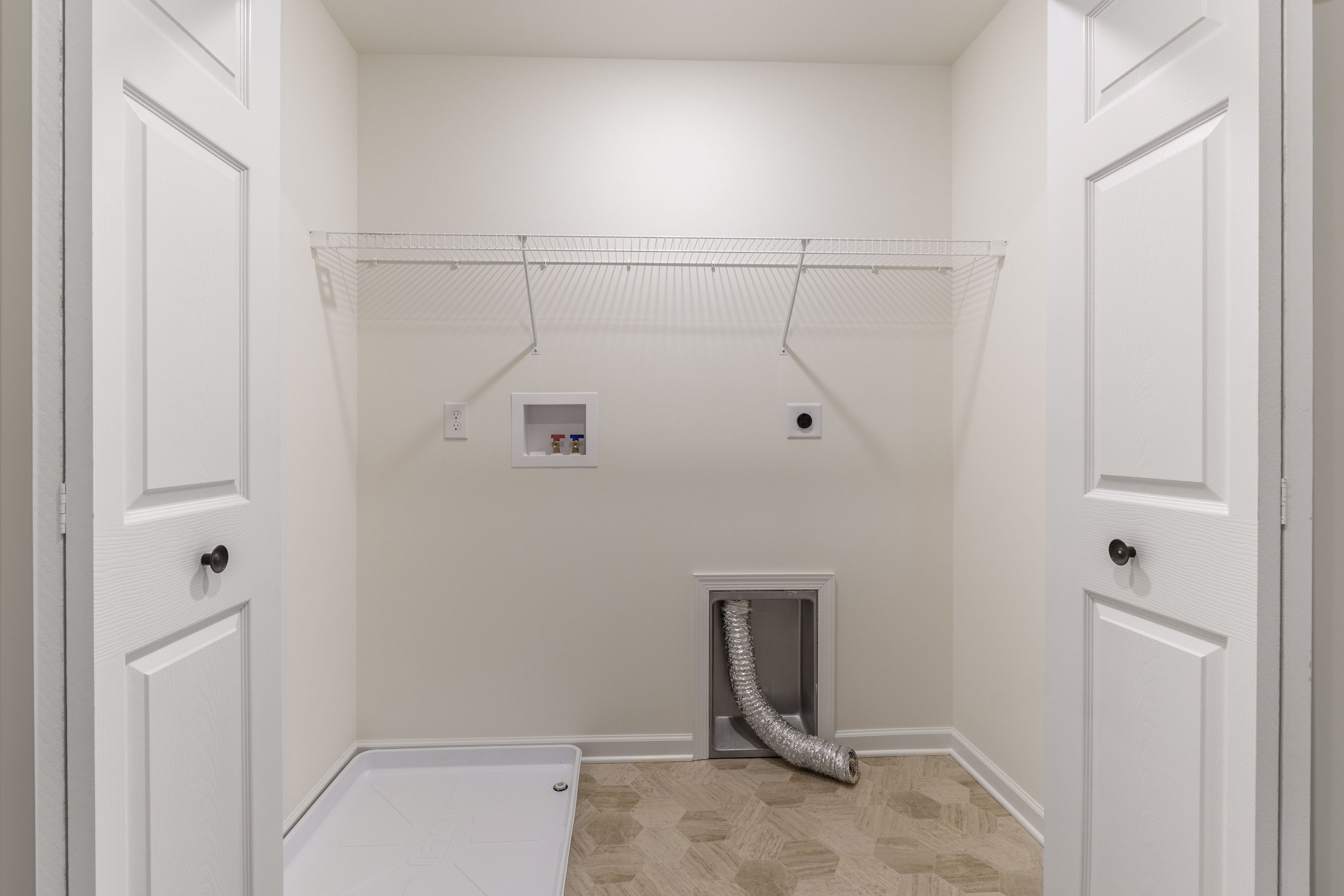 Laundry room with wire shelving, space for washer/dryer, and beige flooring.