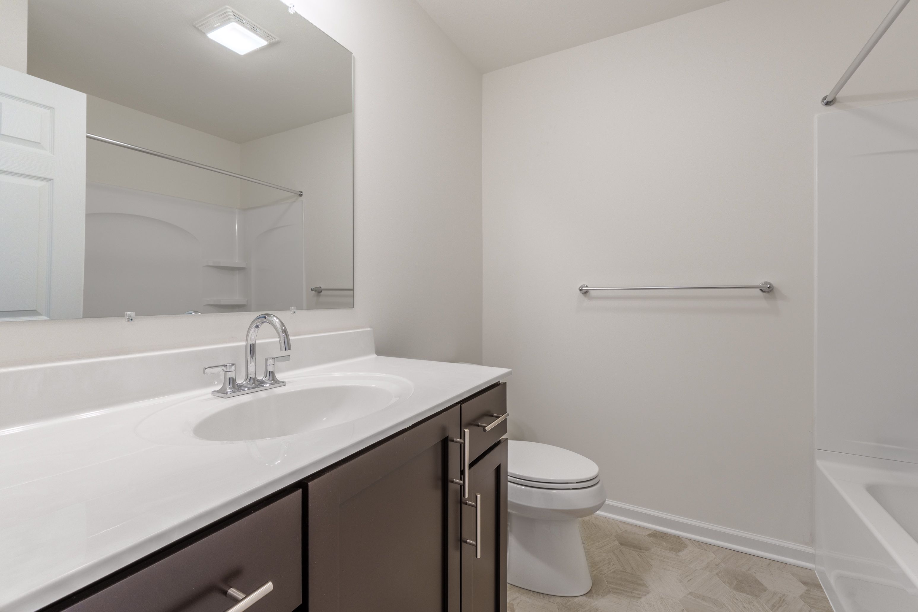 Modern bathroom with a white vanity, mirror, and shower/tub combo. Clean, neutral tones throughout.