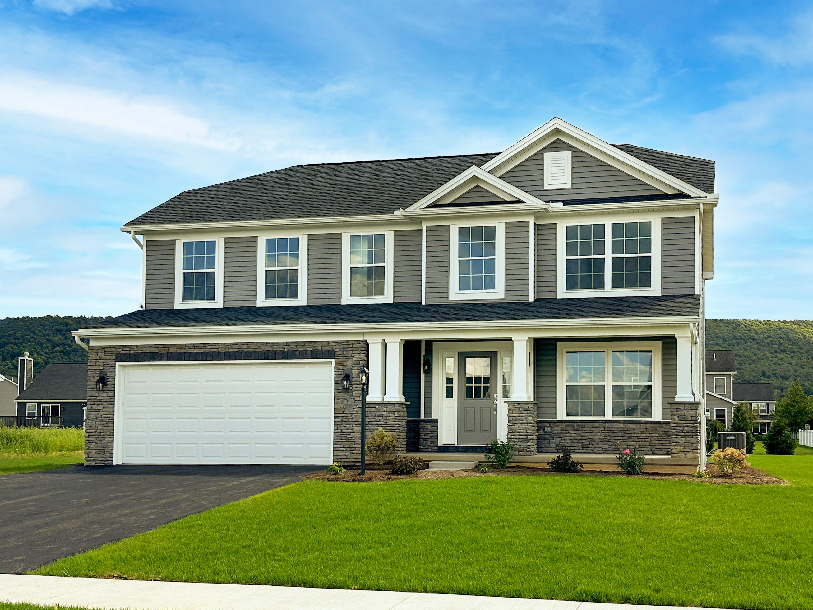 Front view of a two-story home with gray siding, stone accents, white trim, and a double garage