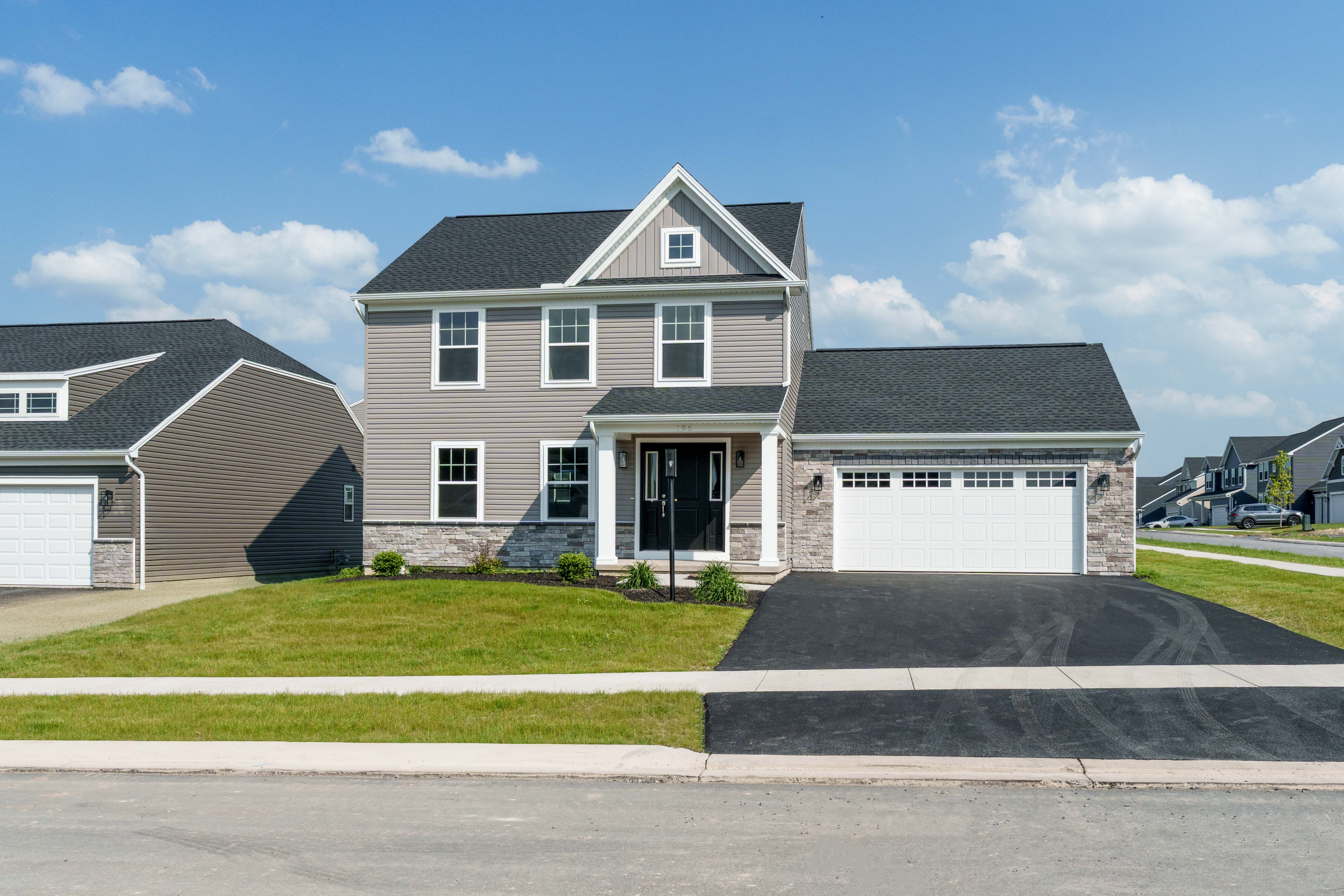 Two-story gray siding home with stone accents, black front door, white trim, and attached two-car garage on a newly paved driveway.