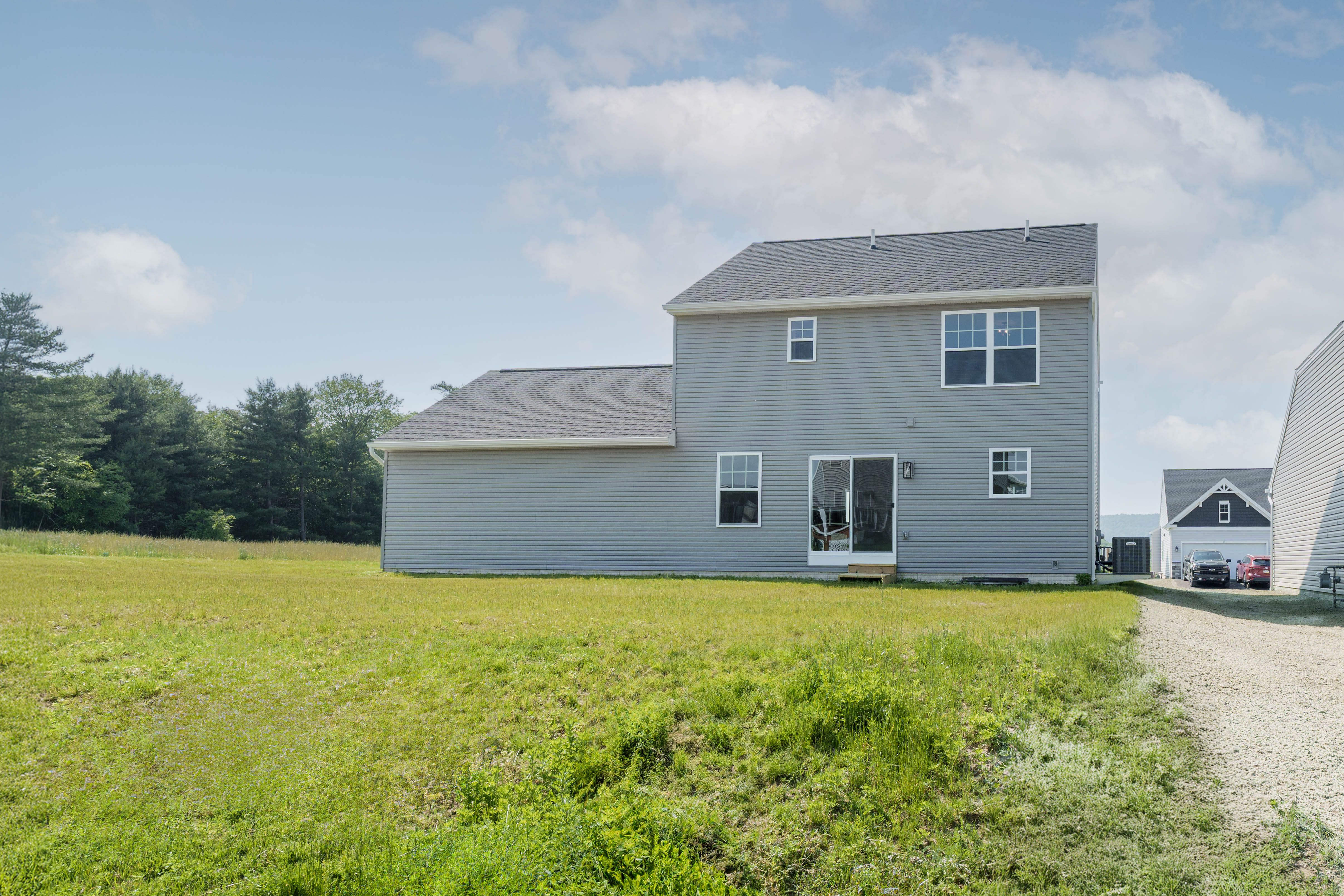 Back view of the home showing gray siding, multiple windows, and a sliding glass door opening to a grassy yard.