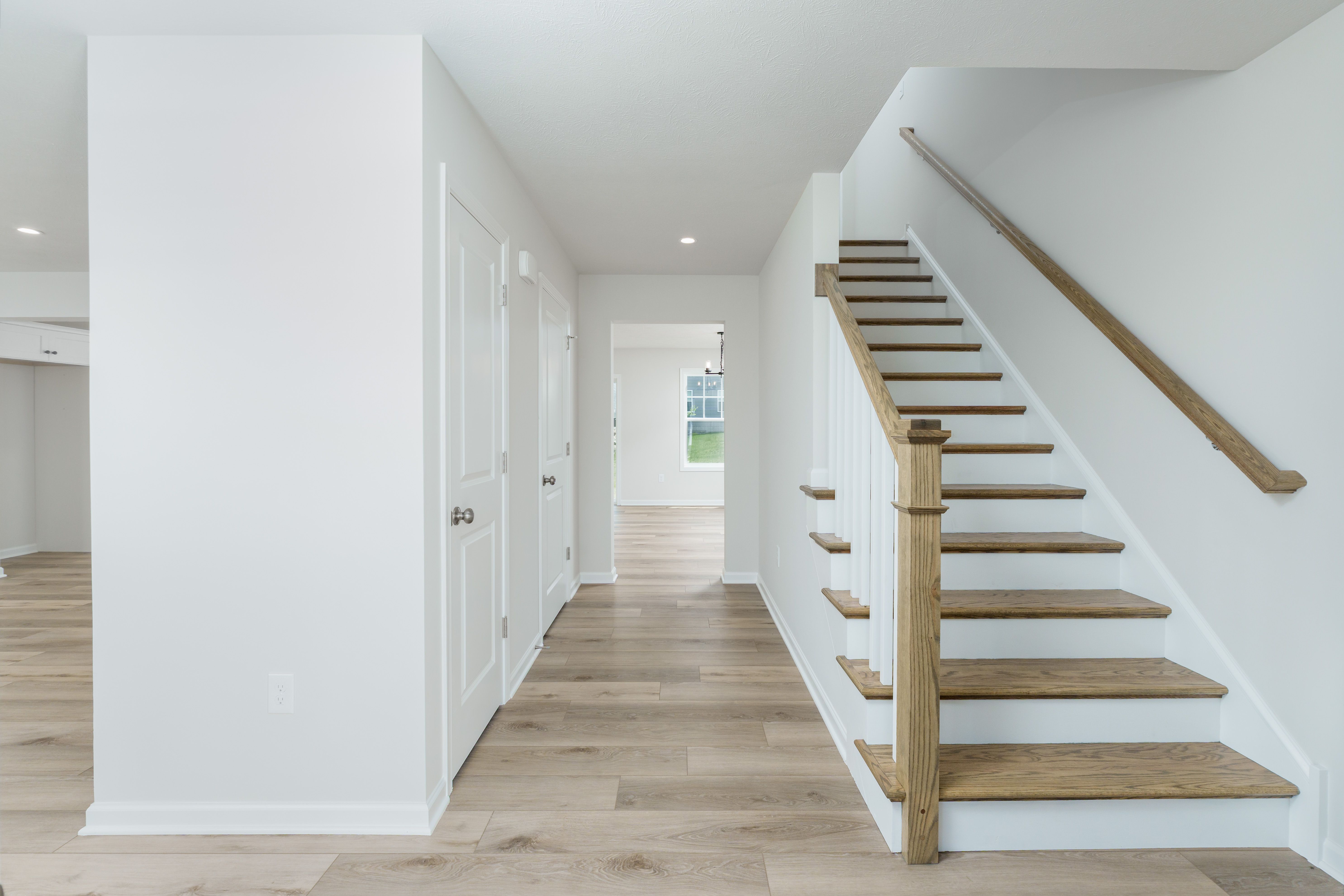 Bright foyer with natural wood stairs, white railing, and luxury vinyl plank floors leading to hallway.