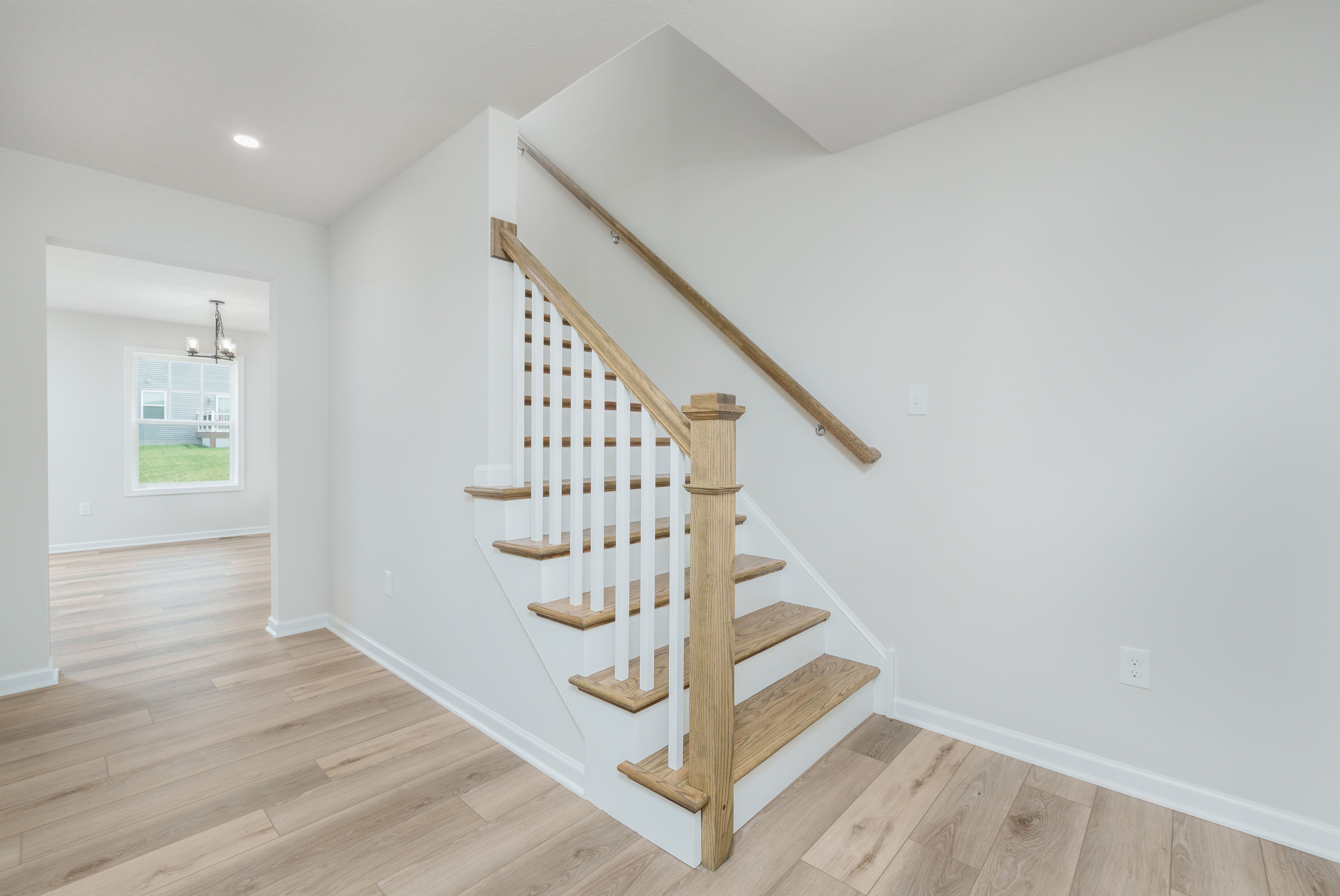 View of staircase with wooden treads and white spindles, next to open room with large back window.