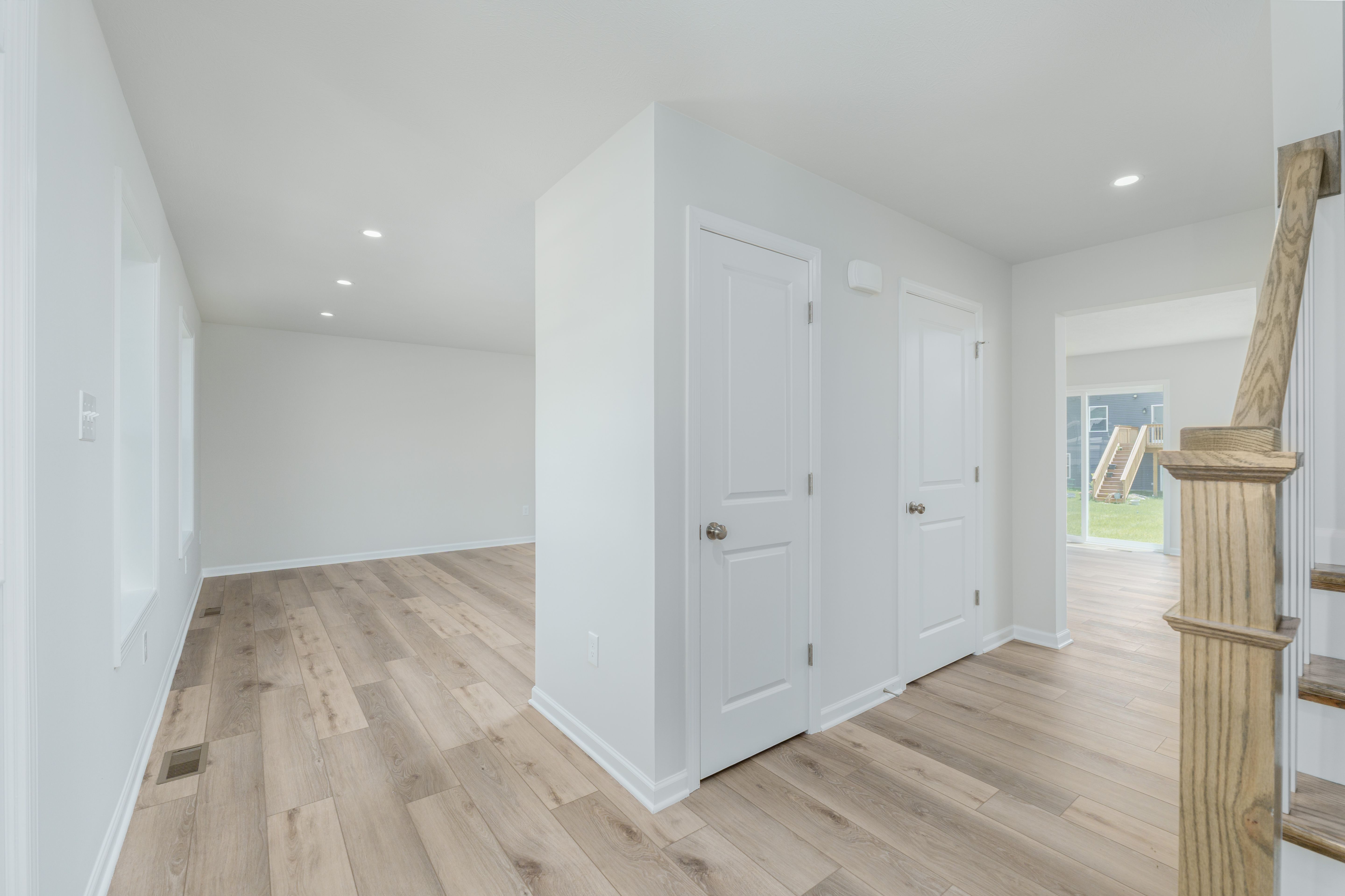 Spacious foyer with white doors, light wood stairs, and view of open floor plan beyond.