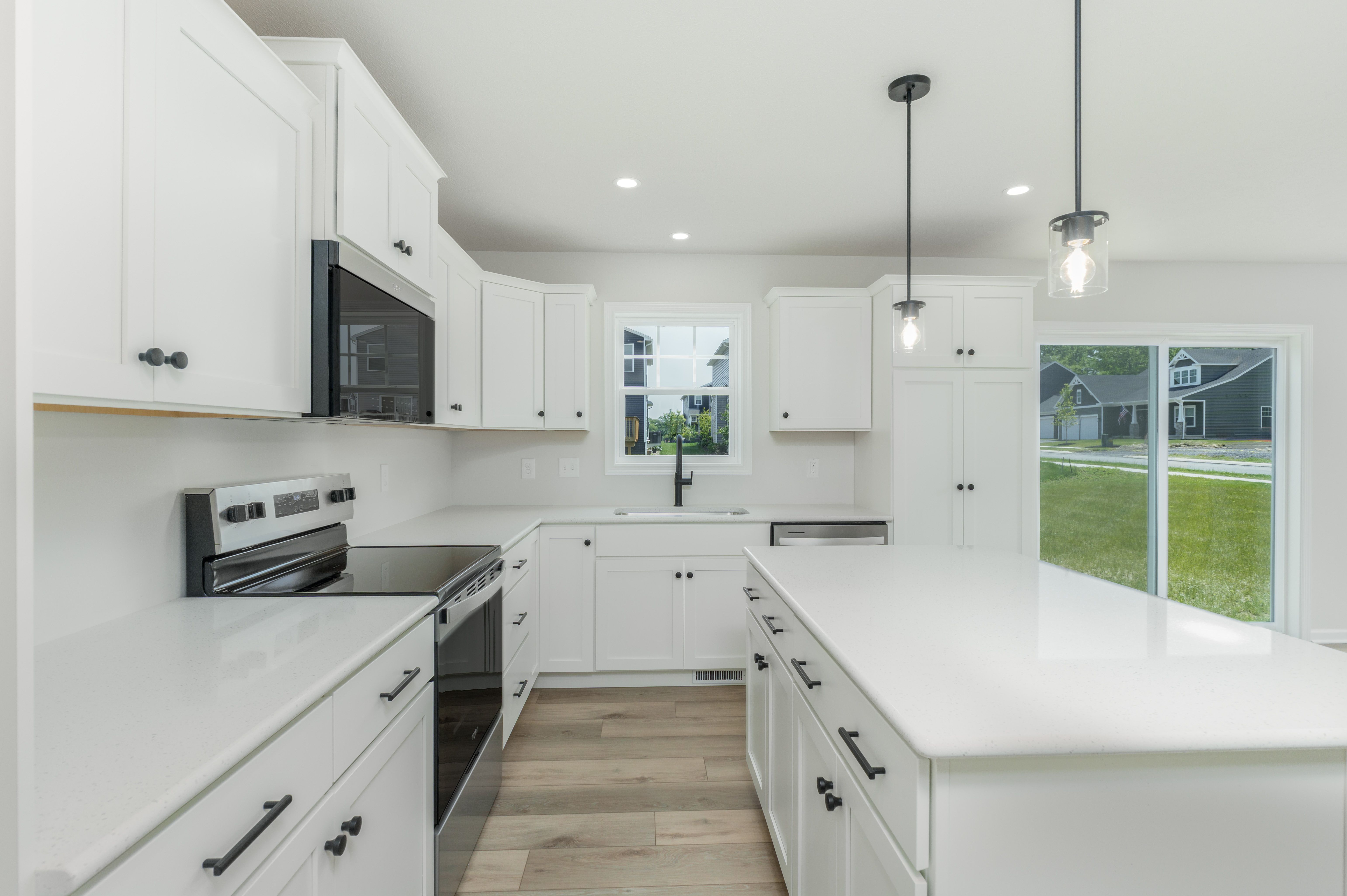 Close-up view of kitchen island, black fixtures, white cabinets, and large window above the sink.