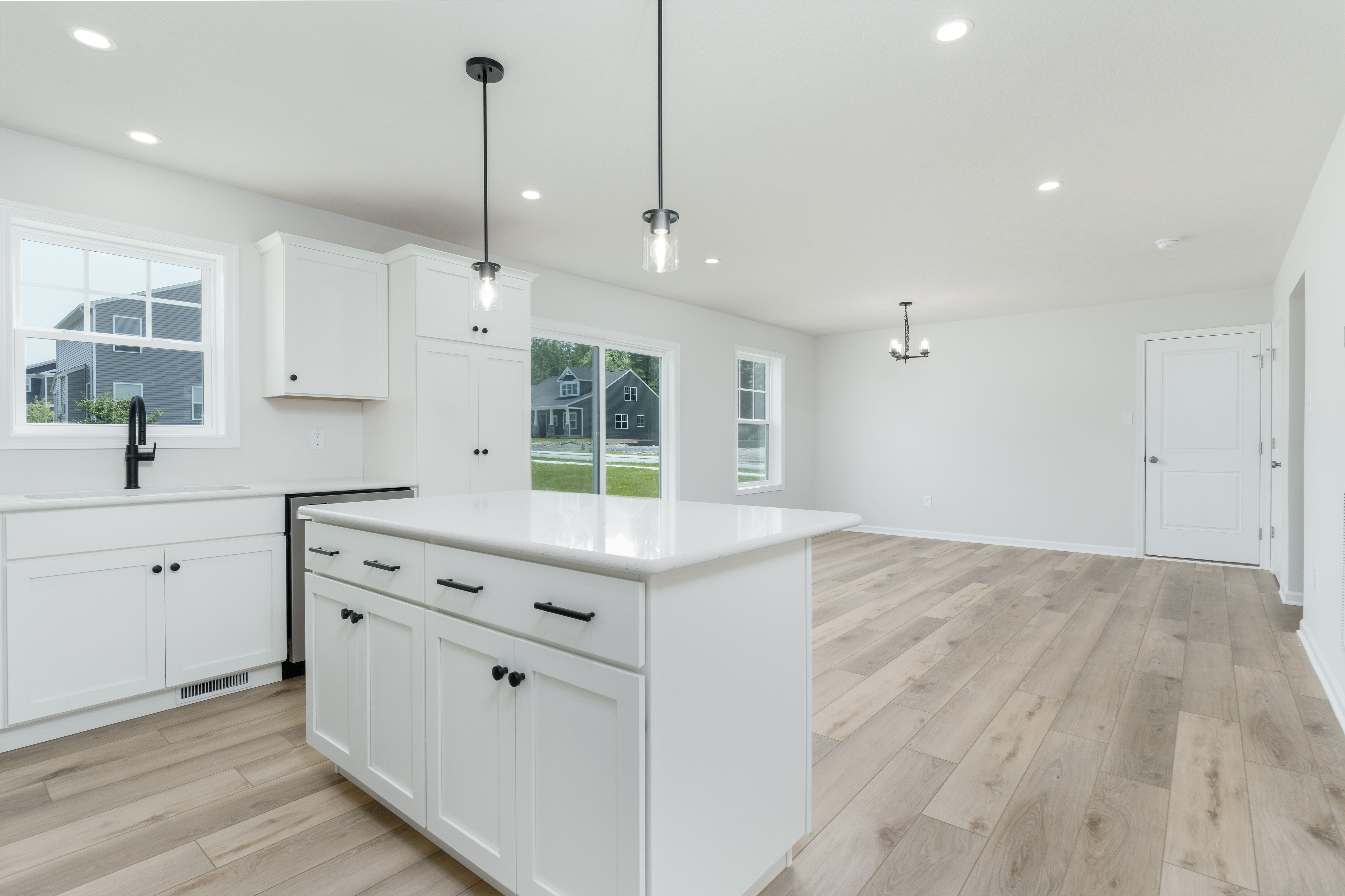 Kitchen island with white quartz top, pendant lights, and open view into breakfast area and backyard.