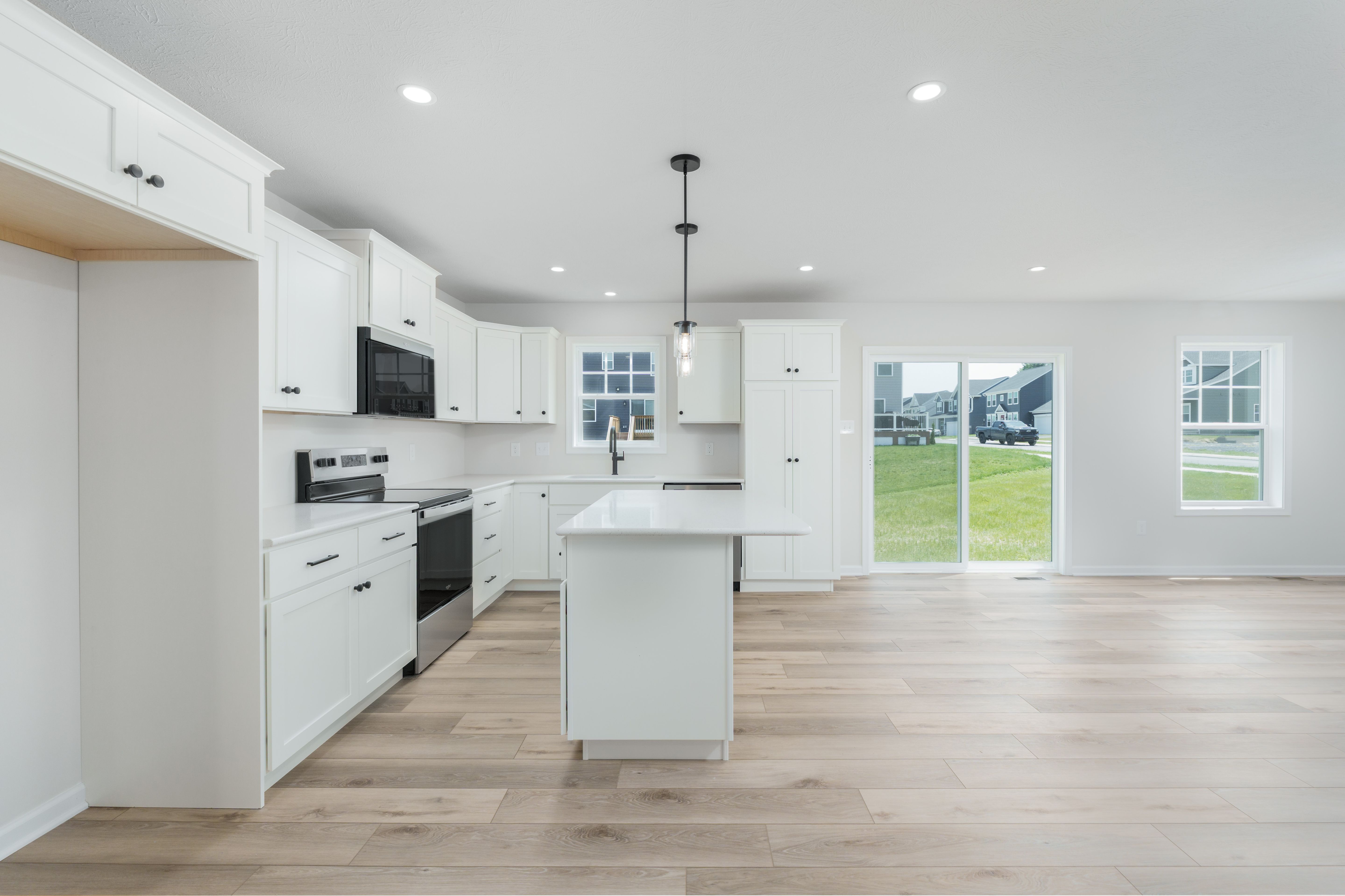 Bright kitchen with white cabinetry, island, pendant lights, and luxury vinyl plank floors opening to backyard.