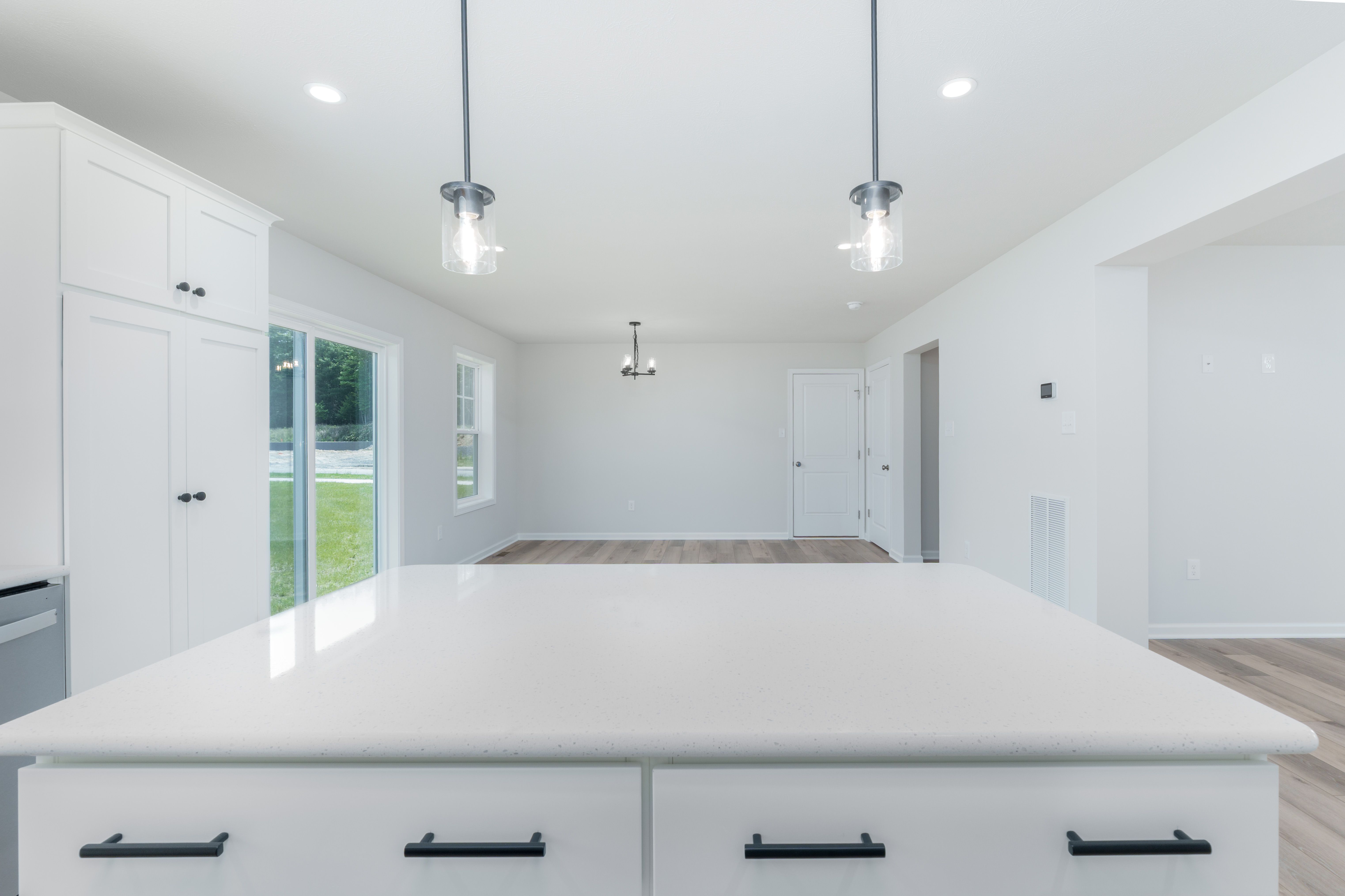 Kitchen island with quartz surface and black hardware, overlooking windows and open floor plan.