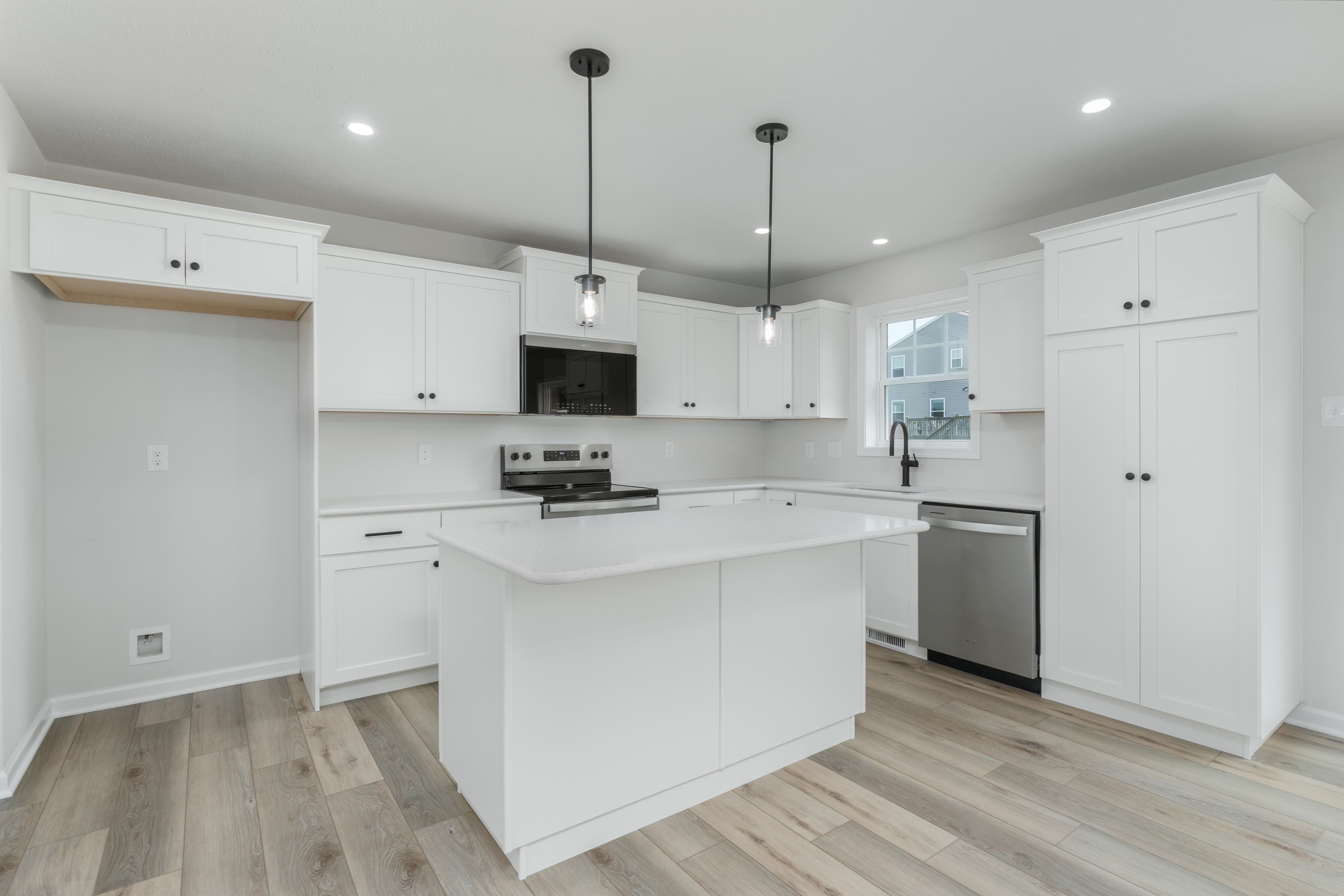 Island-centered kitchen with pendant lighting, black fixtures, and white shaker cabinets throughout.
