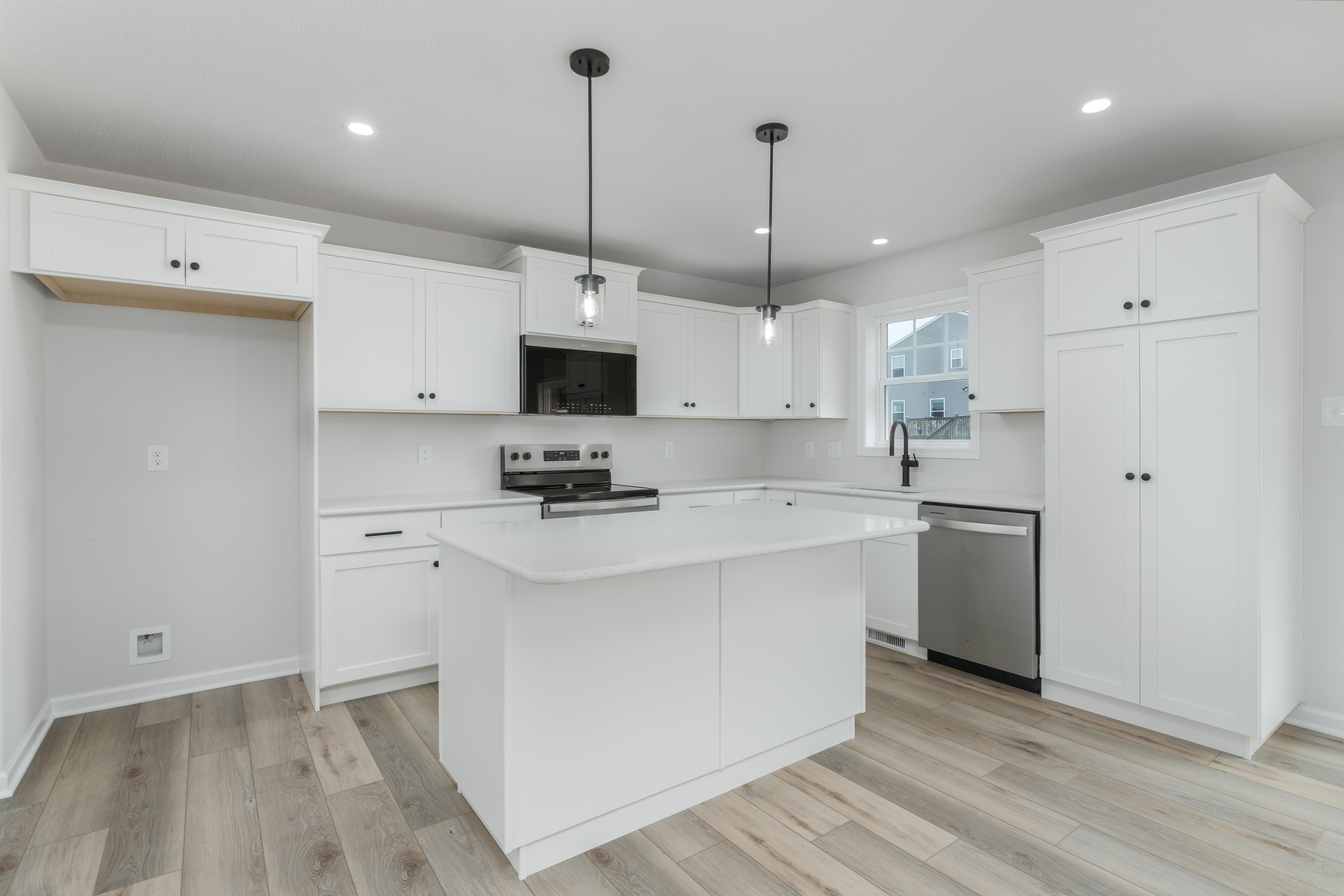 Island-centered kitchen with pendant lighting, black fixtures, and white shaker cabinets throughout.