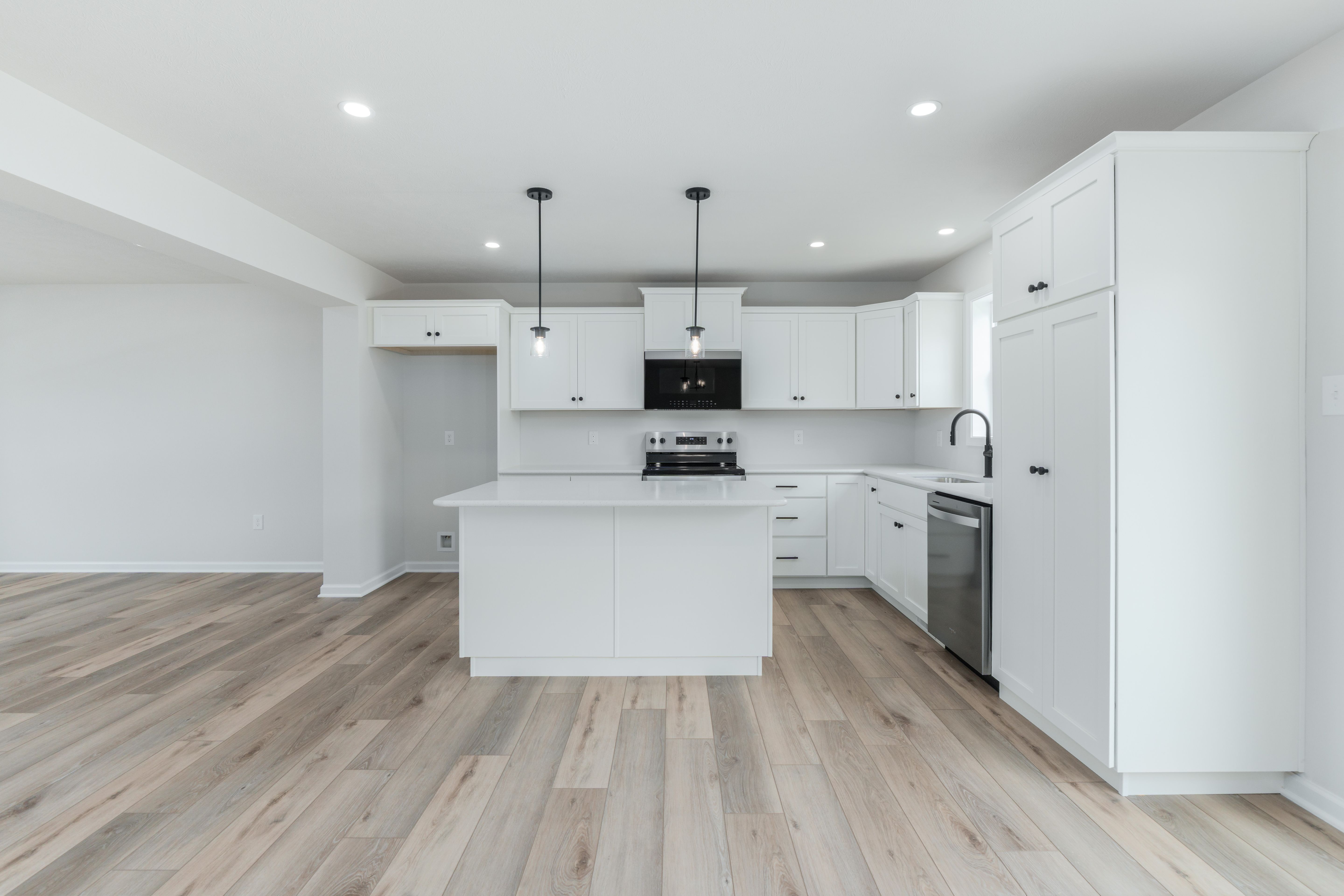 Wide-angle of kitchen with stainless steel appliances, white cabinets, and island with black hardware.