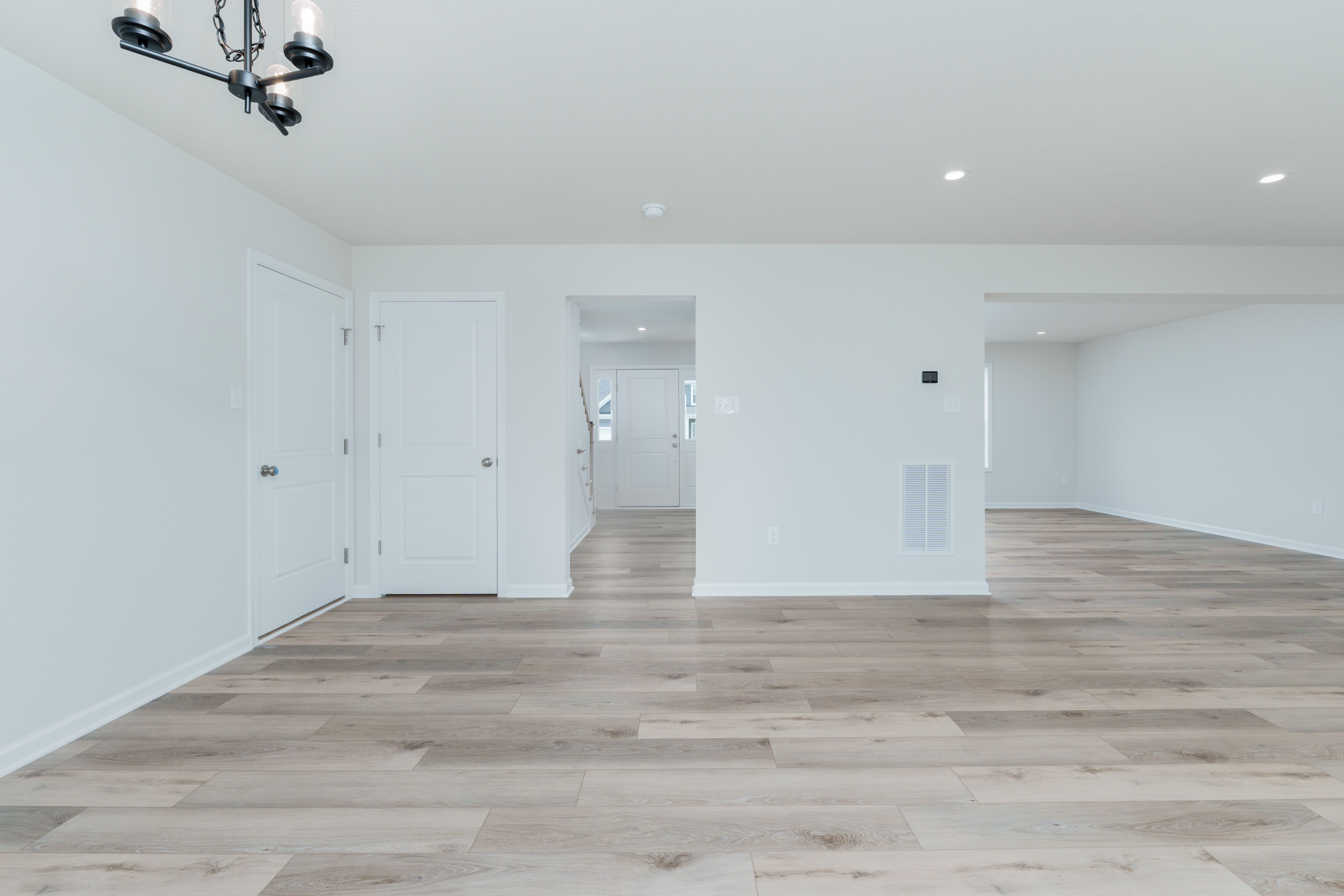 Dining area off kitchen with black chandelier, white double doors, and light wood flooring throughout.