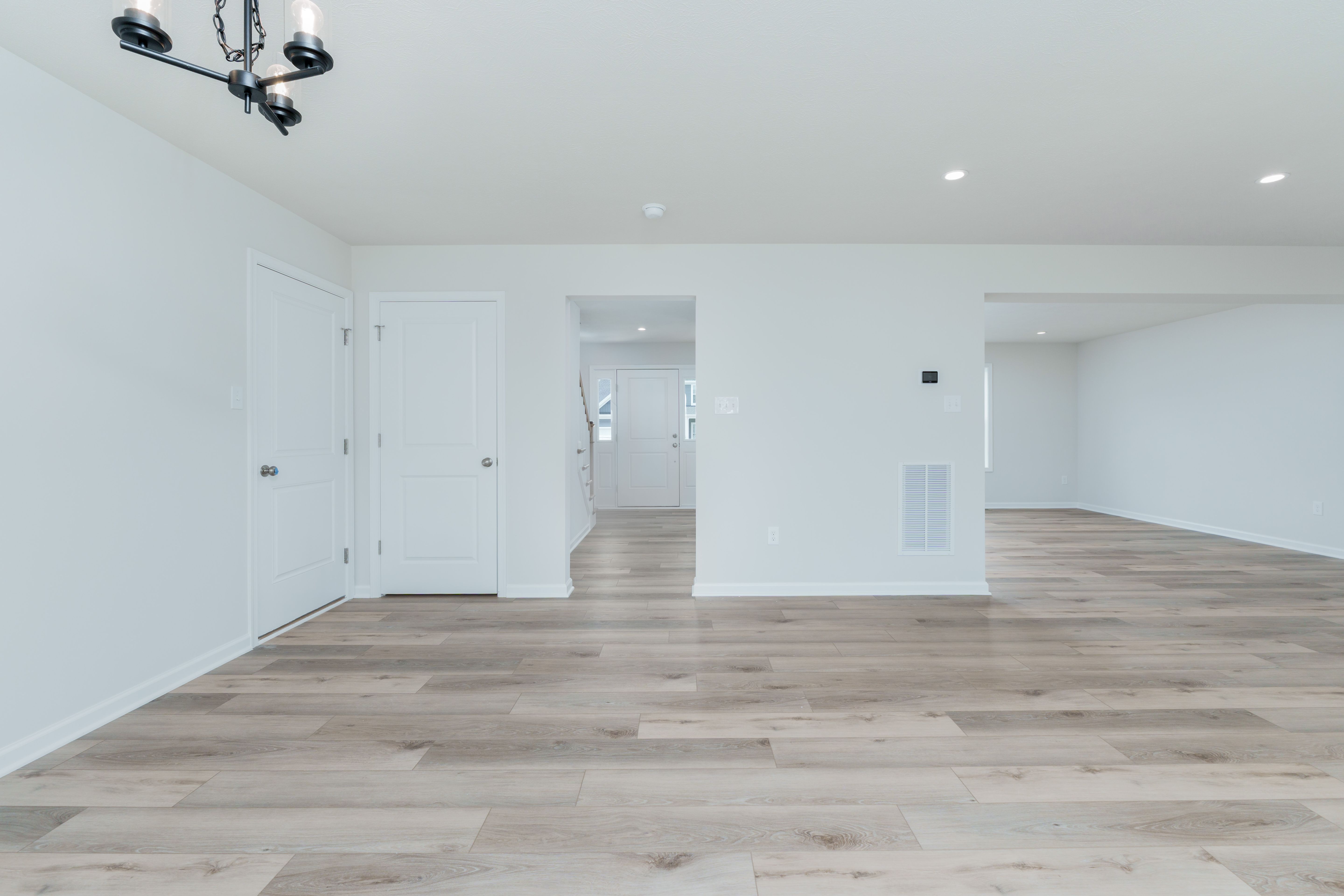 Dining area off kitchen with black chandelier, white double doors, and light wood flooring throughout.