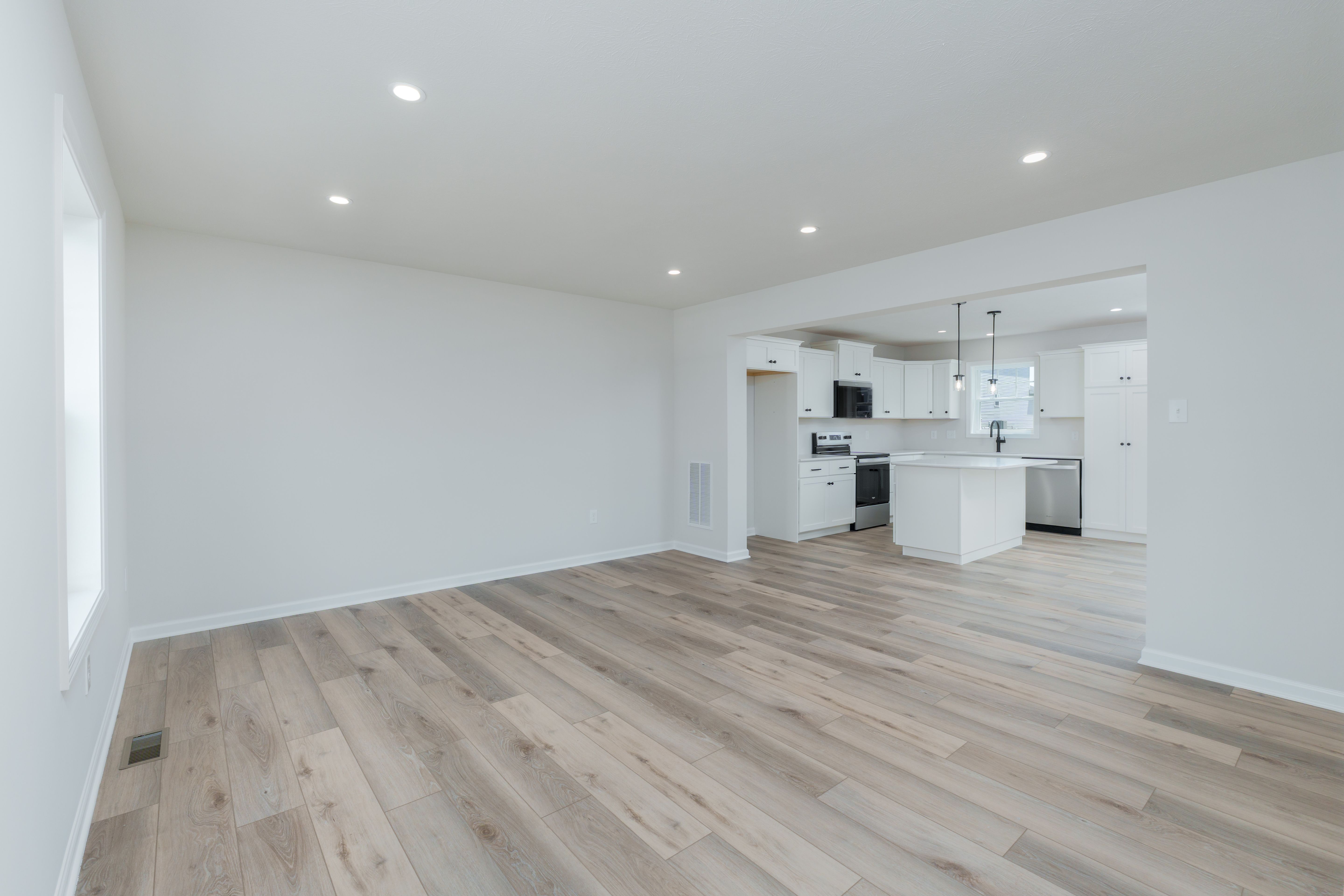 Open family room with luxury vinyl plank flooring, recessed lighting, and view into a white kitchen with island.