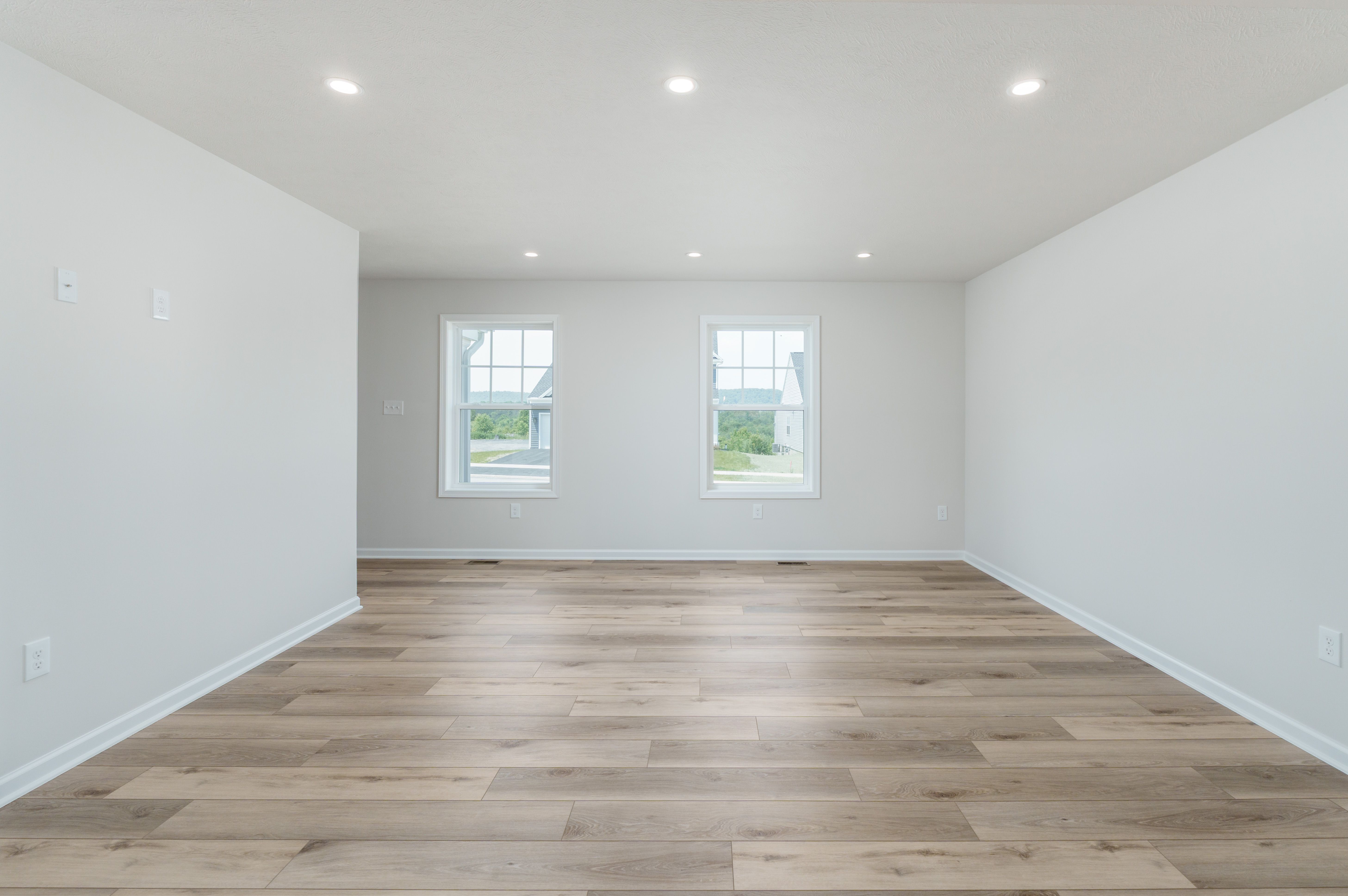 Family room with luxury vinyl plank flooring, two windows, white walls, and natural light.