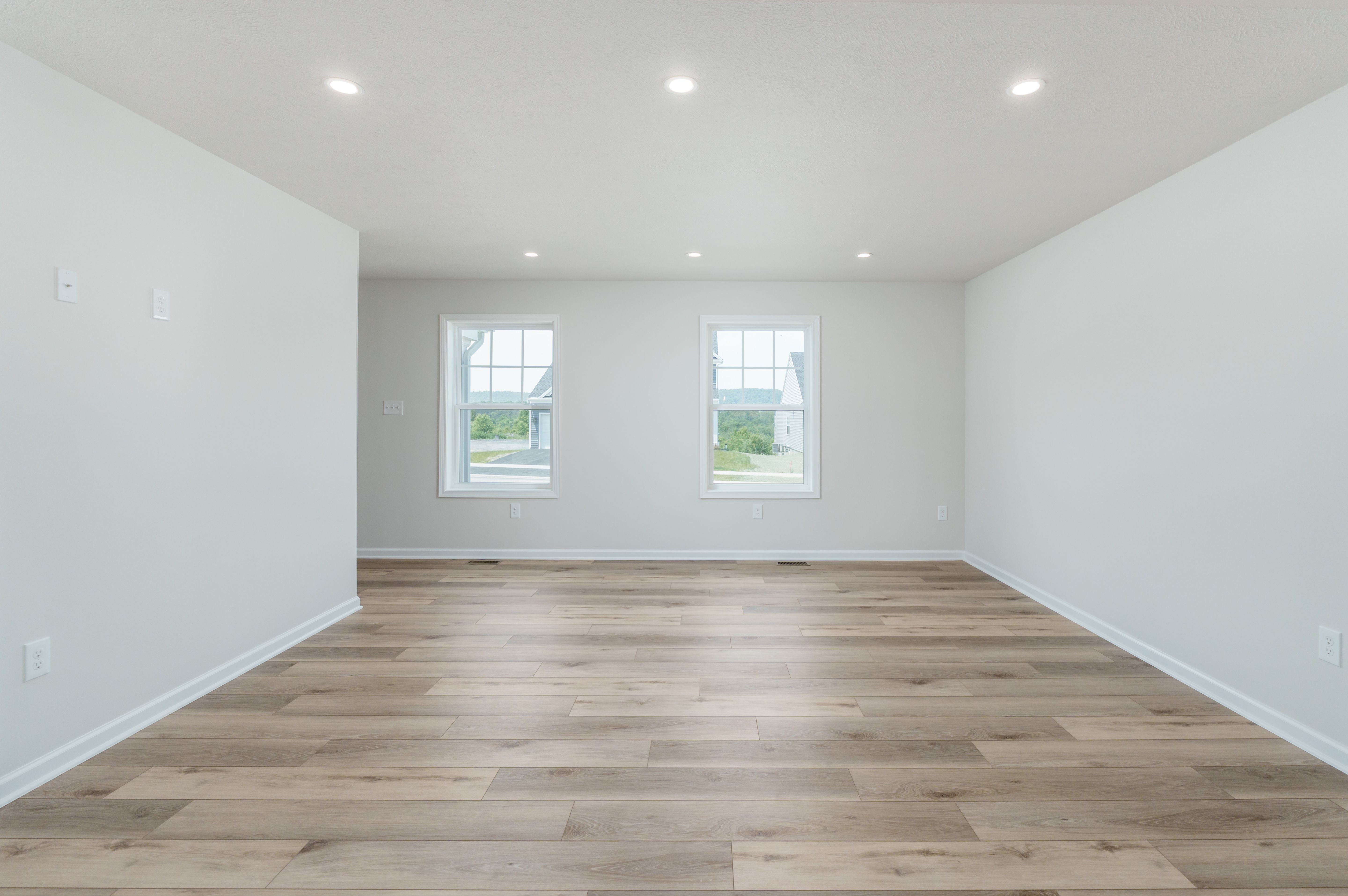 Family room with luxury vinyl plank flooring, two windows, white walls, and natural light.