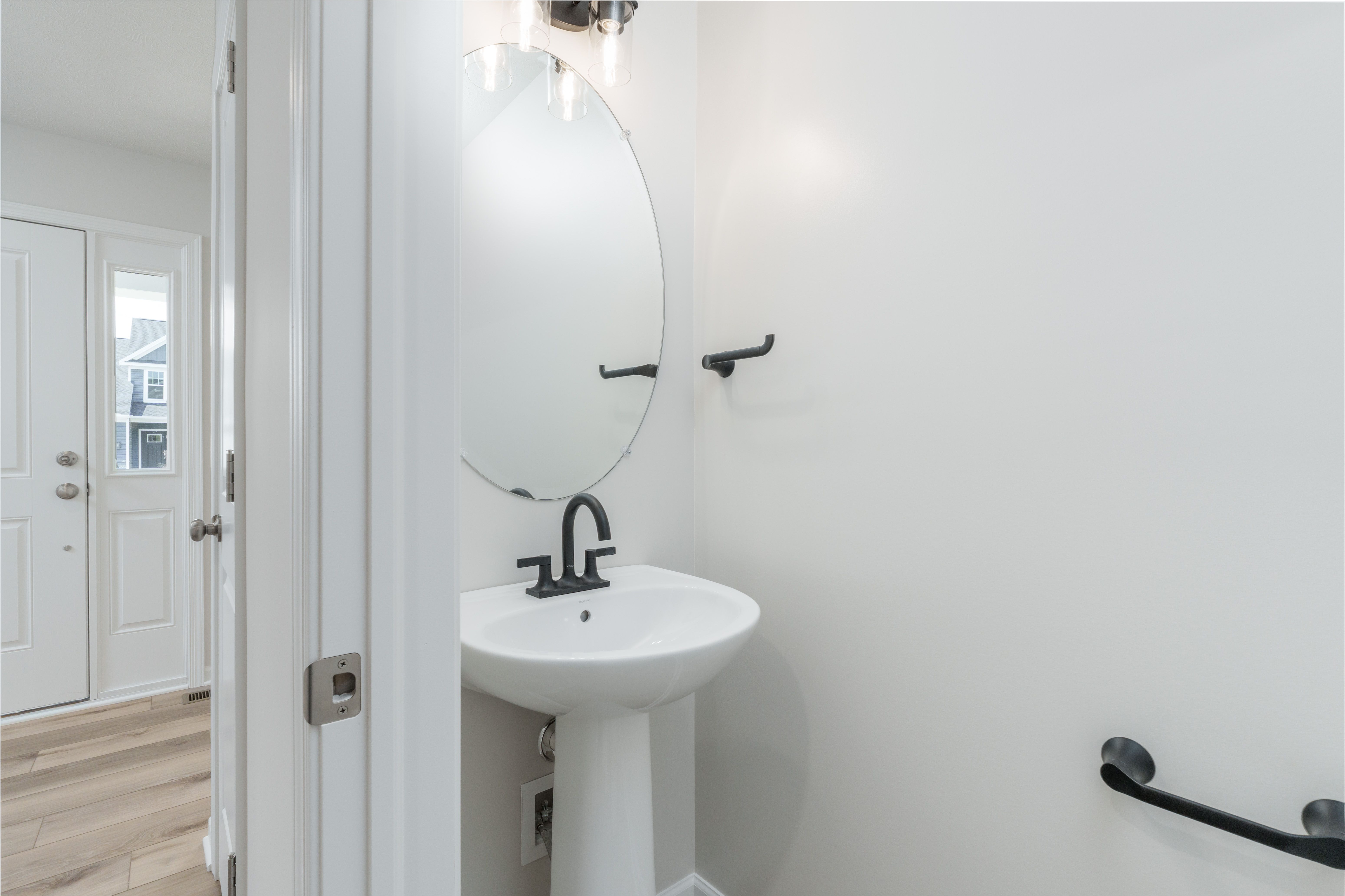 First-floor powder room with pedestal sink, oval mirror, and black light fixture near entryway.