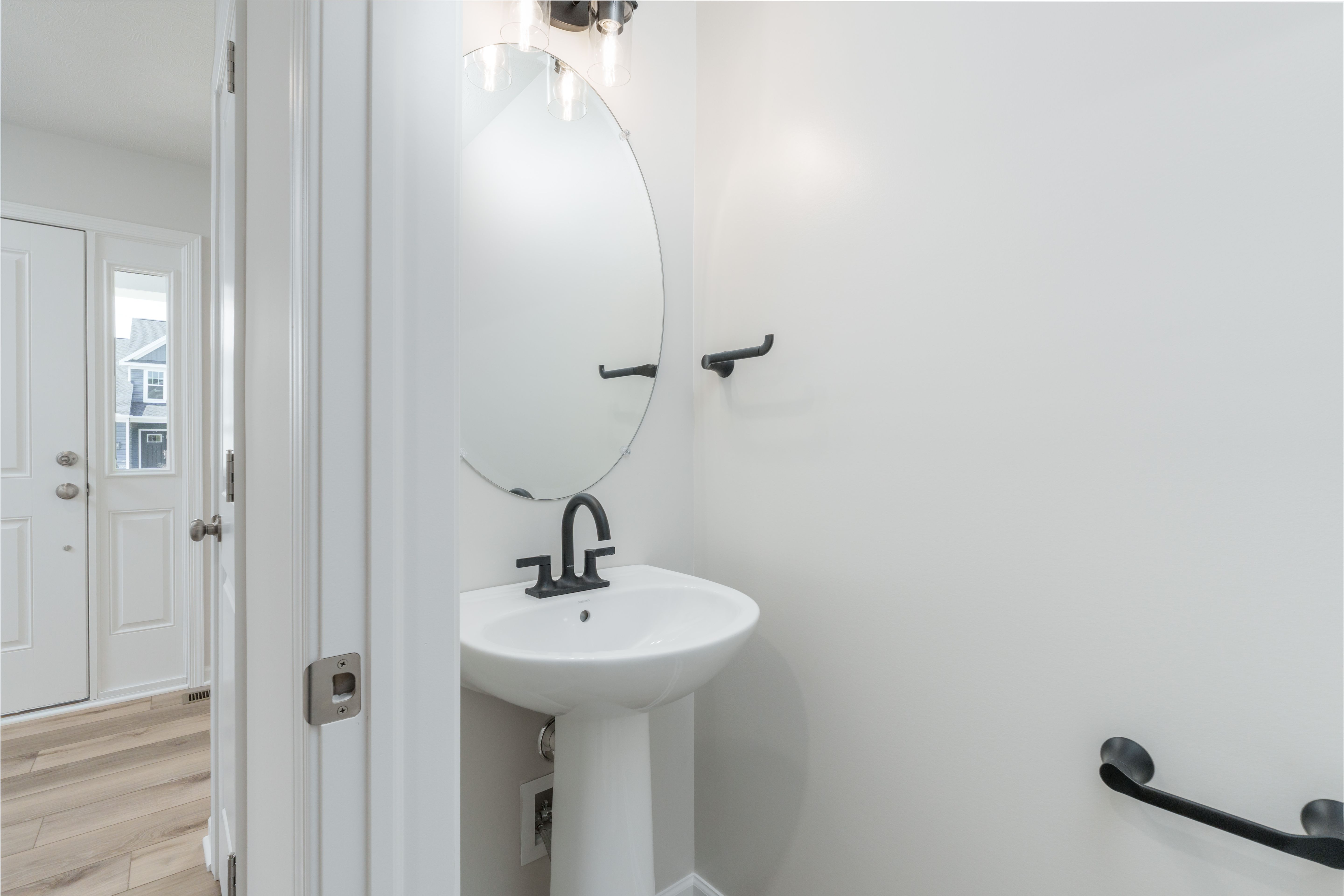 First-floor powder room with pedestal sink, oval mirror, and black light fixture near entryway.