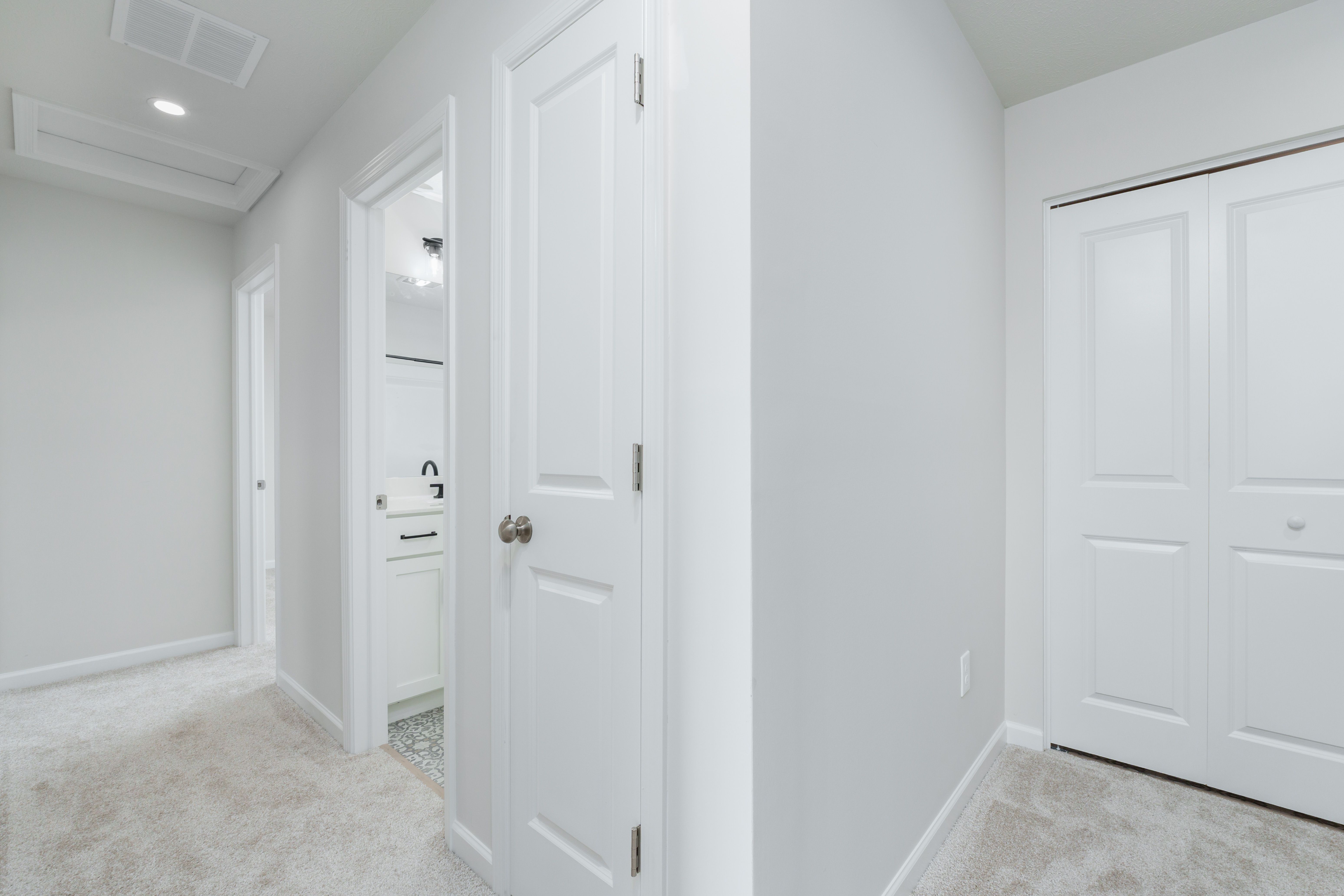 Carpeted upper hallway with multiple white doors, including a bathroom entry and double-door closet.