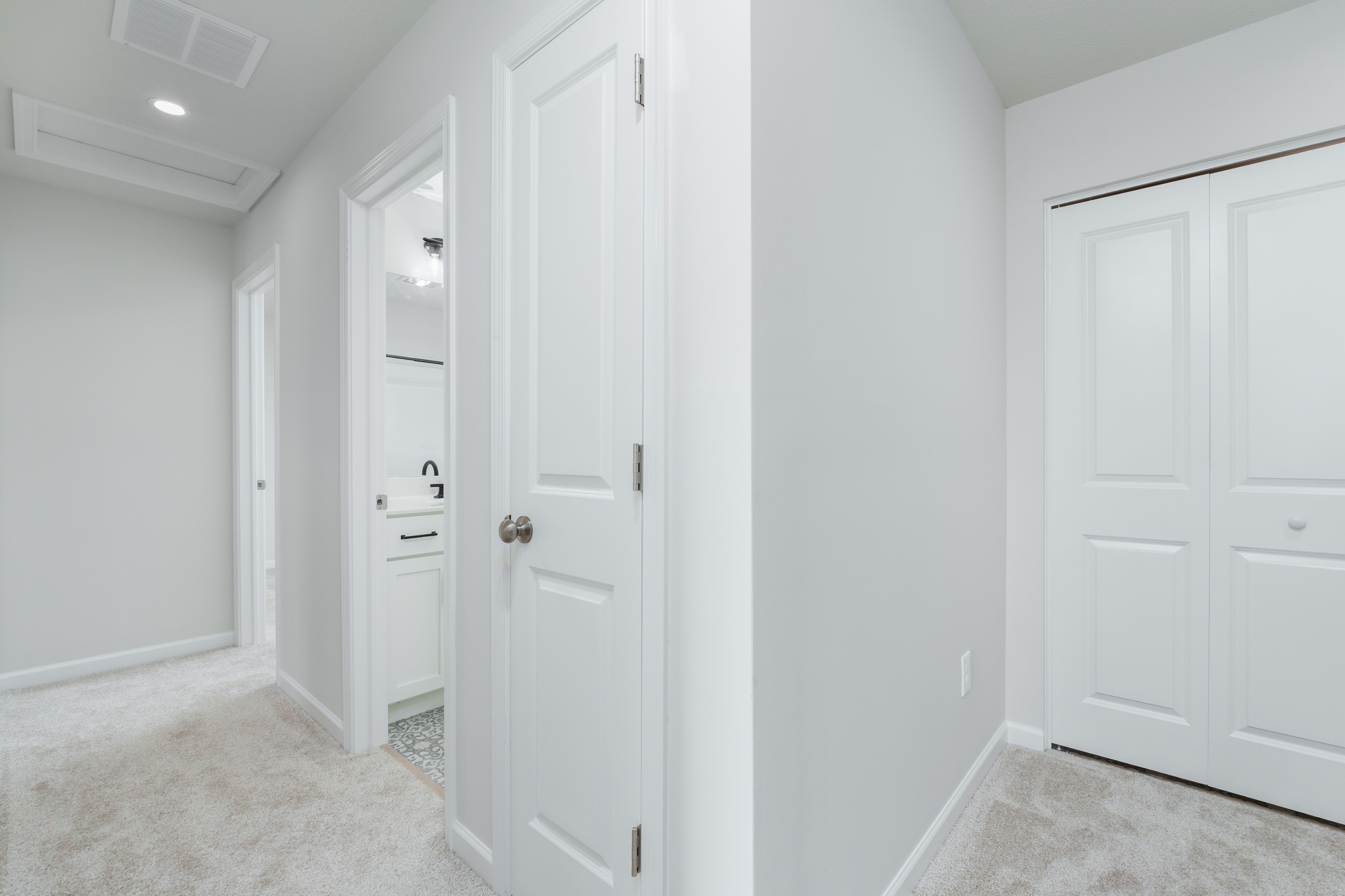 Carpeted upper hallway with multiple white doors, including a bathroom entry and double-door closet.