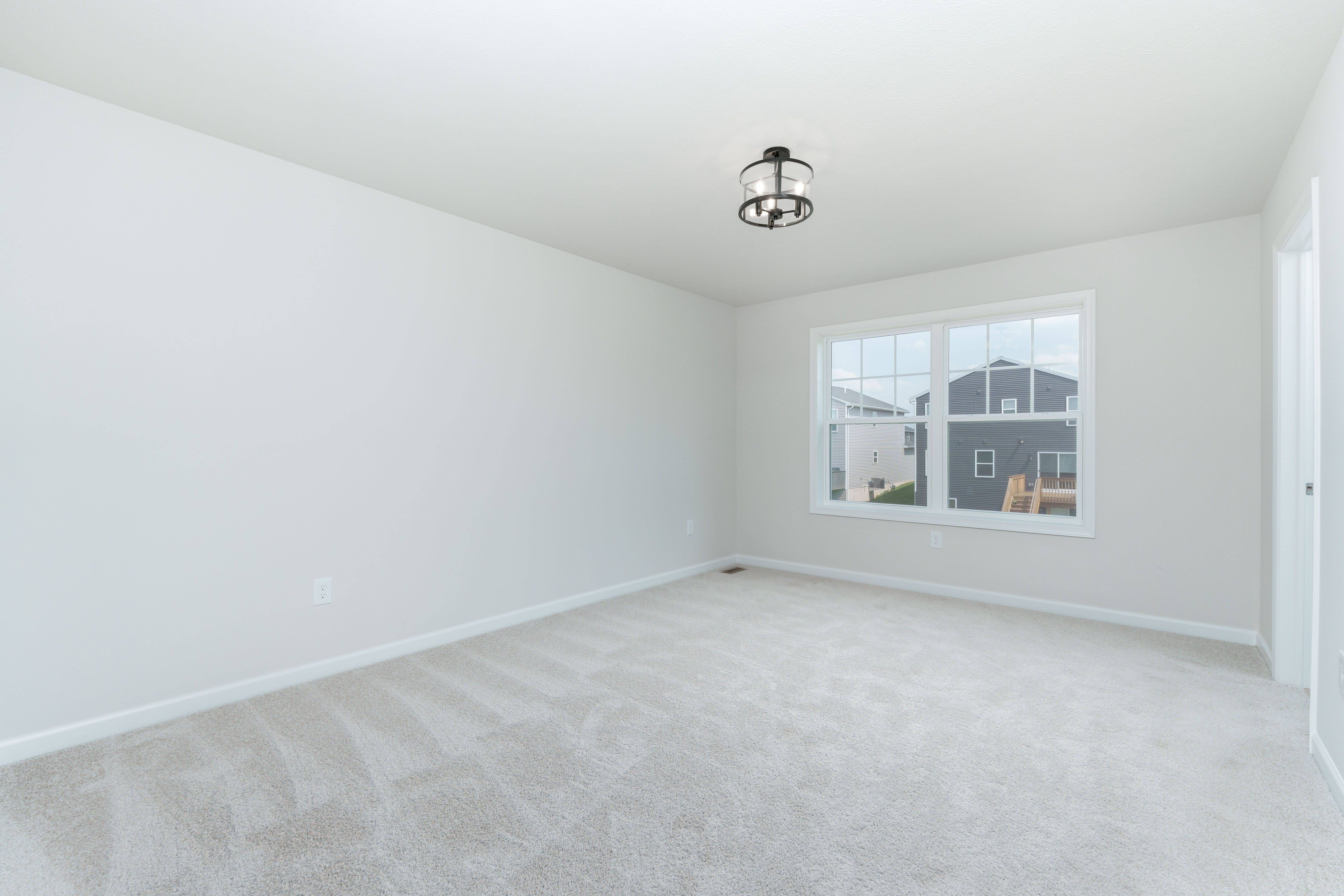 Spacious bedroom with plush carpet, large double window, and modern black cage light.