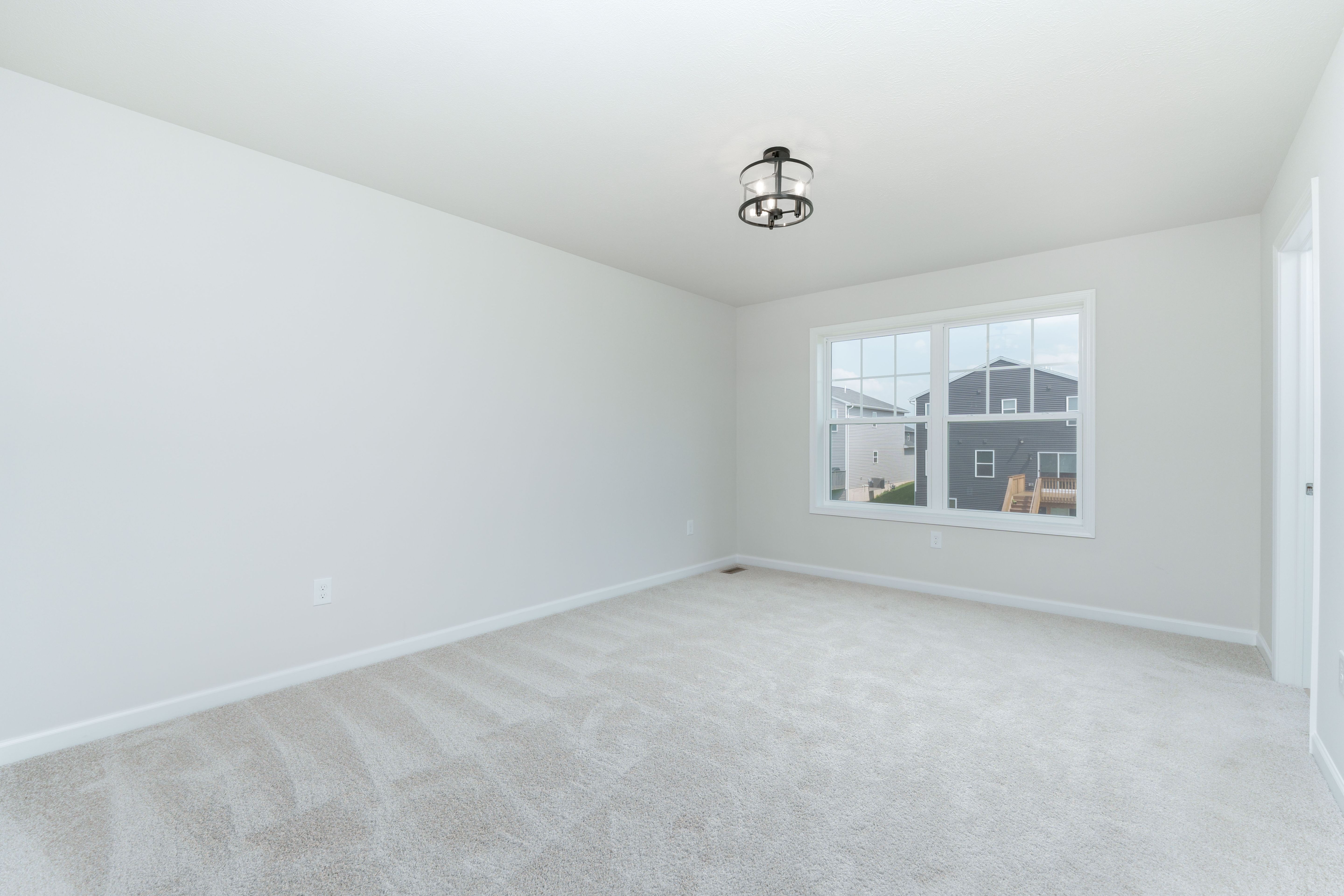 Spacious bedroom with plush carpet, large double window, and modern black cage light.