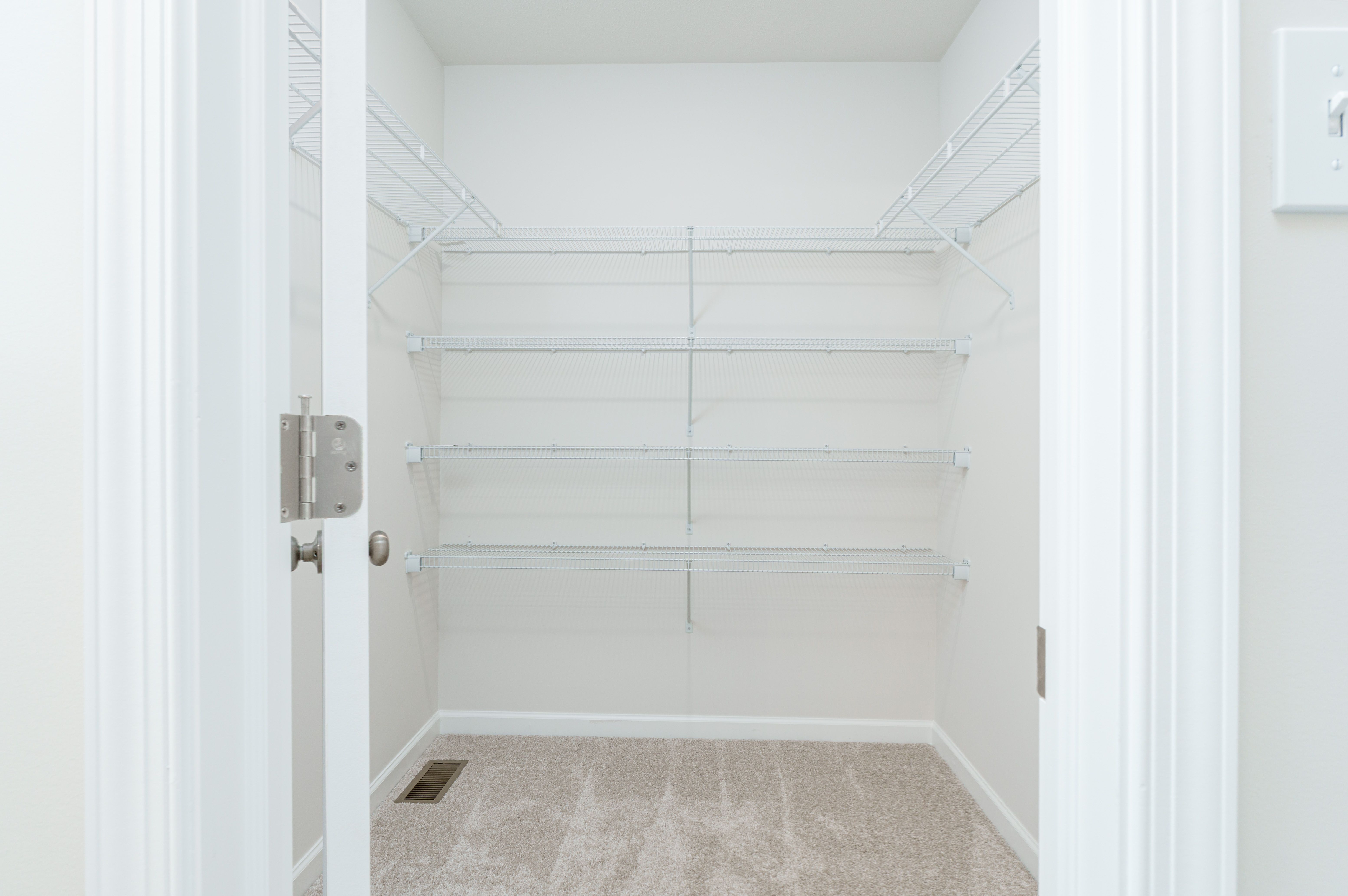 Walk-in closet with beige carpet and white wire shelving on three walls for ample storage.