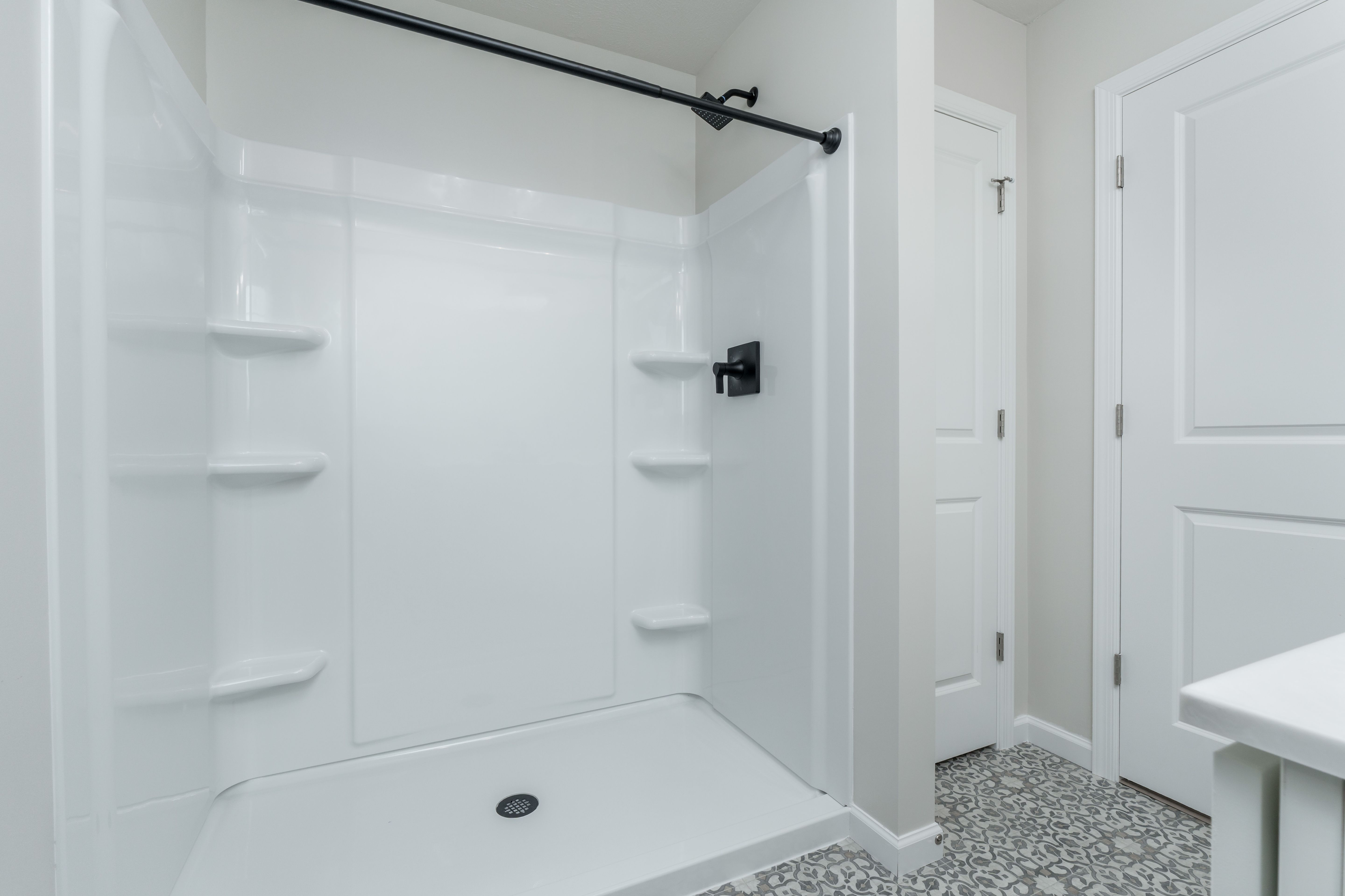 White fiberglass shower with black showerhead, curtain rod, and built-in corner shelves.