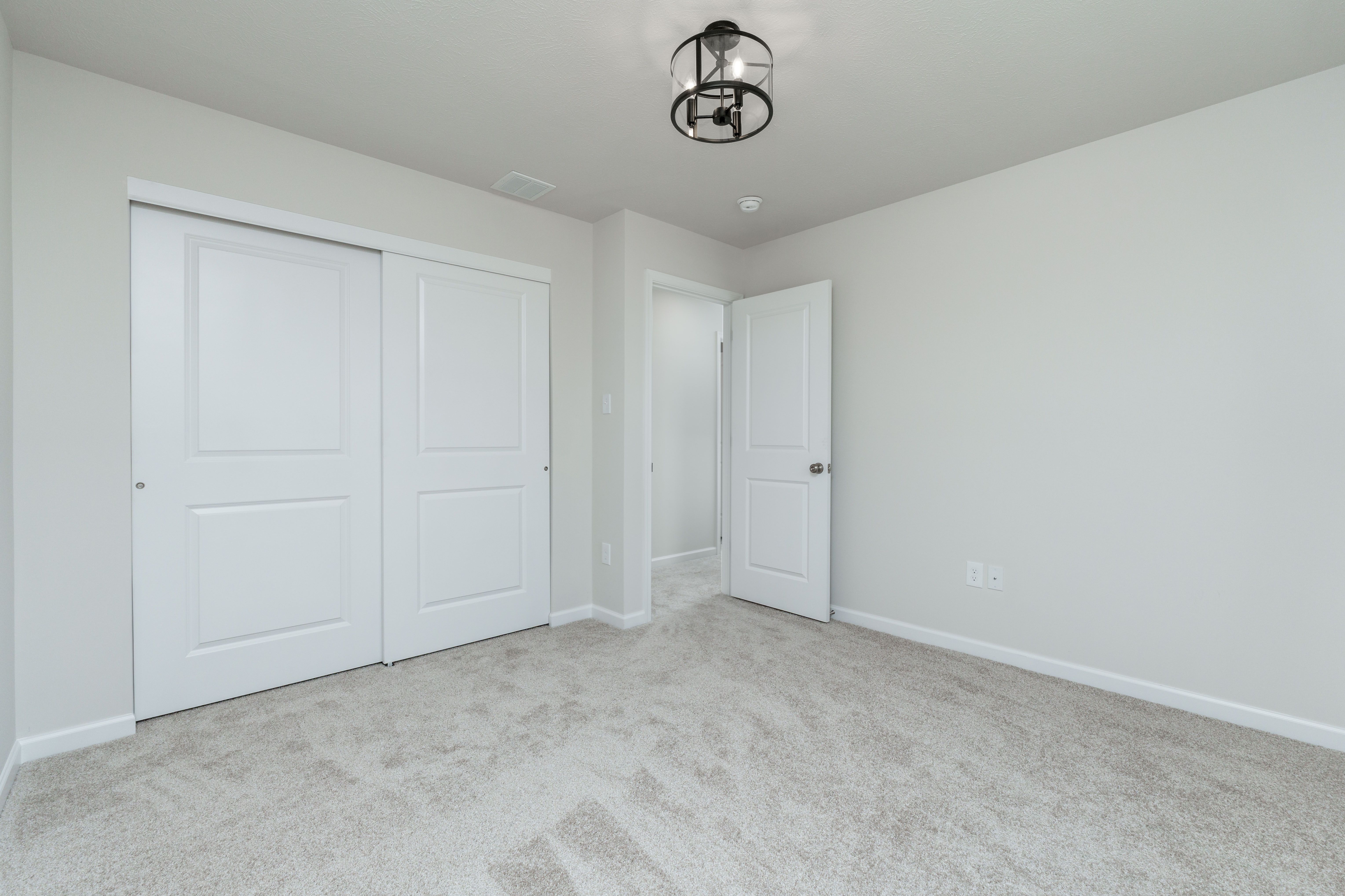 Carpeted bedroom with sliding double-door closet, ceiling light, and open door to hallway.