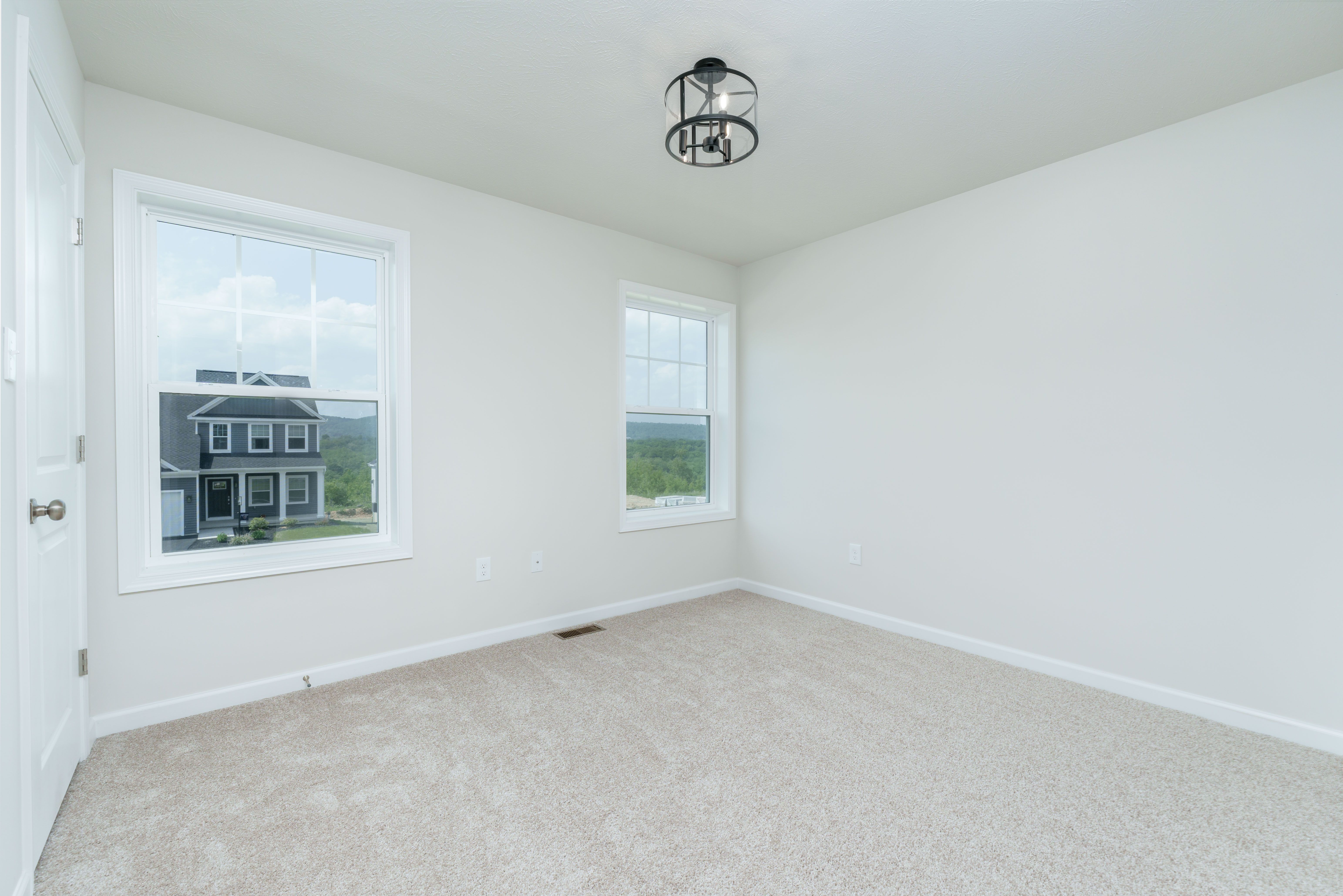 Bedroom with two windows, beige carpet, white trim, and a view of a neighboring home and open sky.