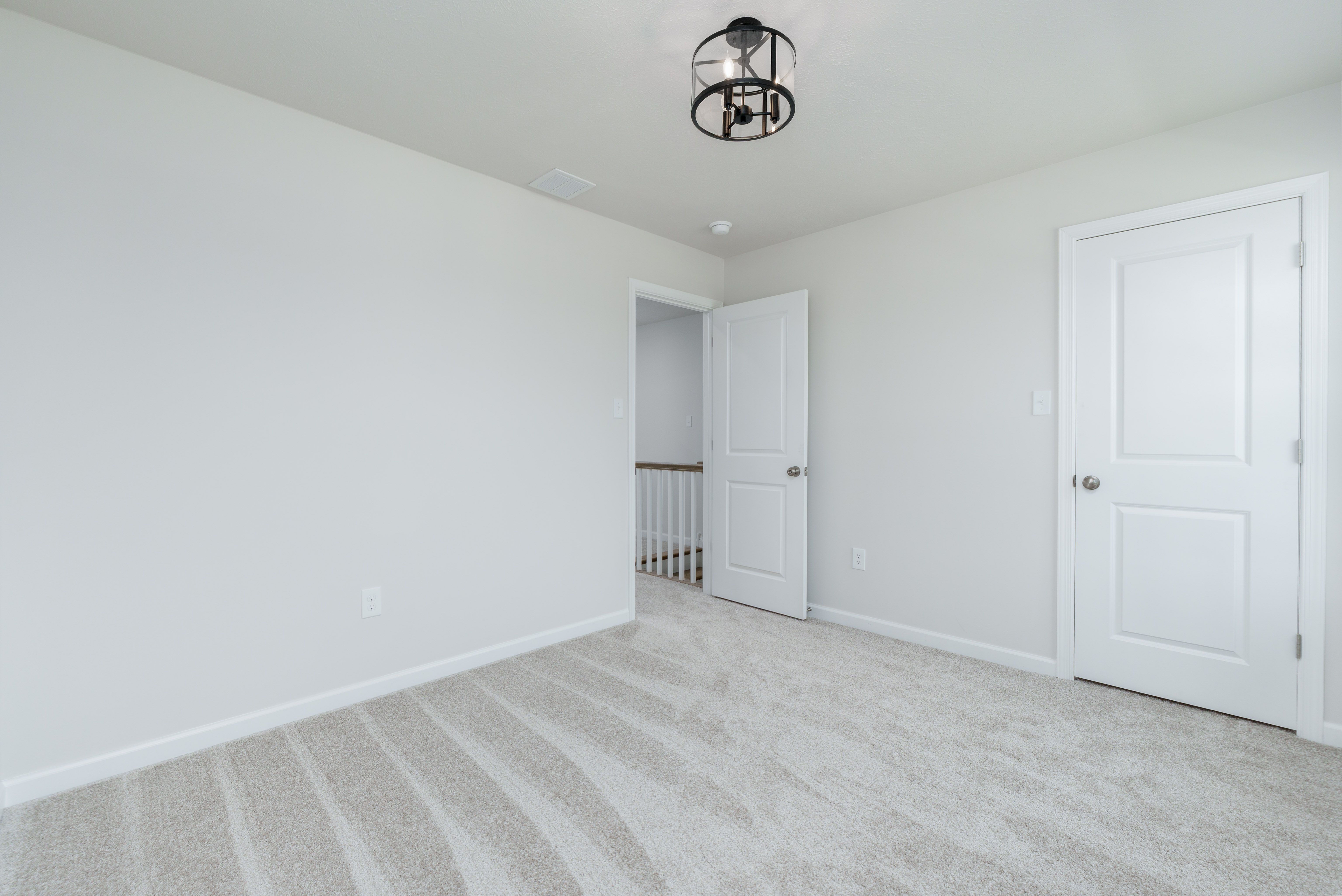 Bedroom with beige carpet, two white doors, and view into upstairs hallway with white railing.