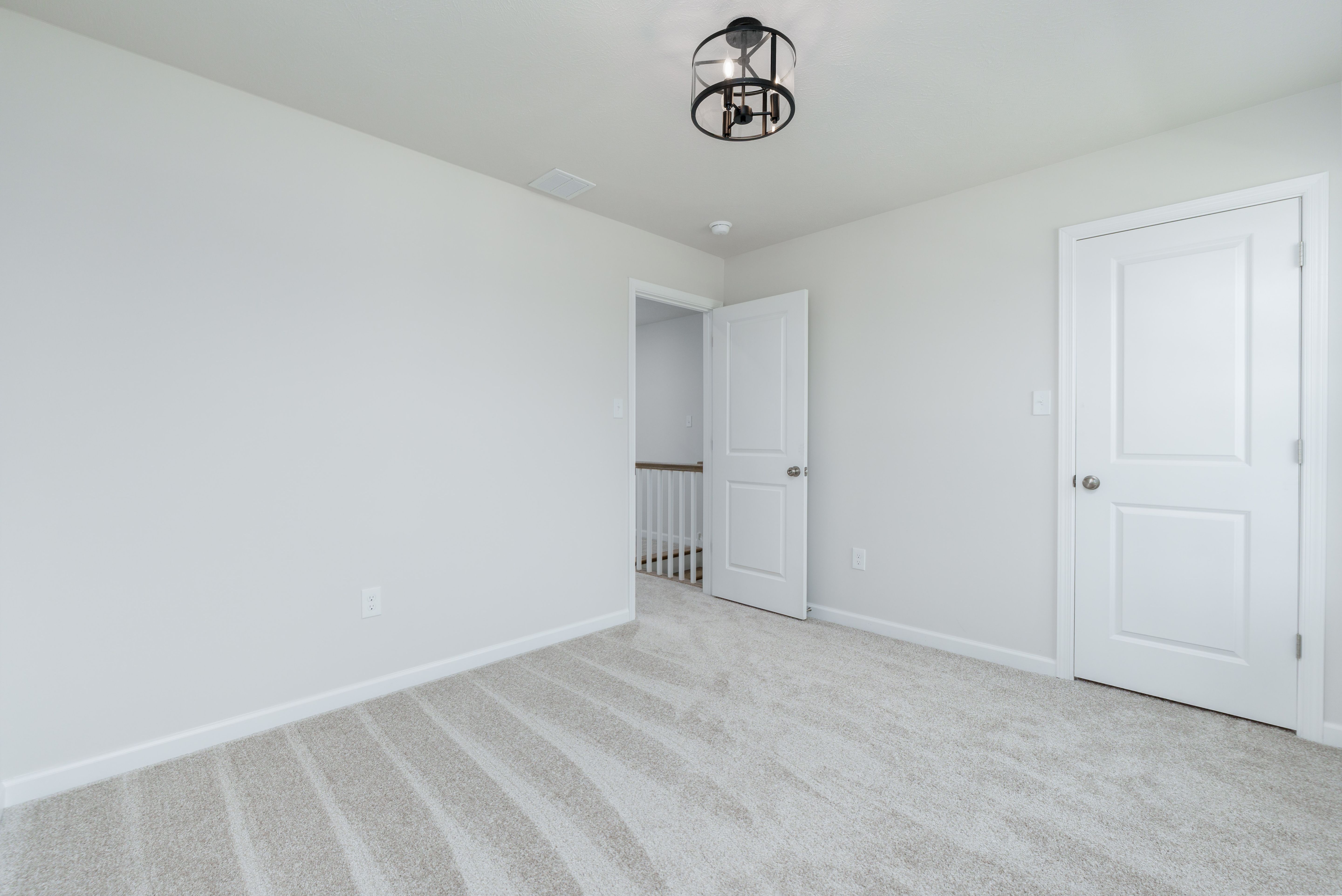 Bedroom with beige carpet, two white doors, and view into upstairs hallway with white railing.